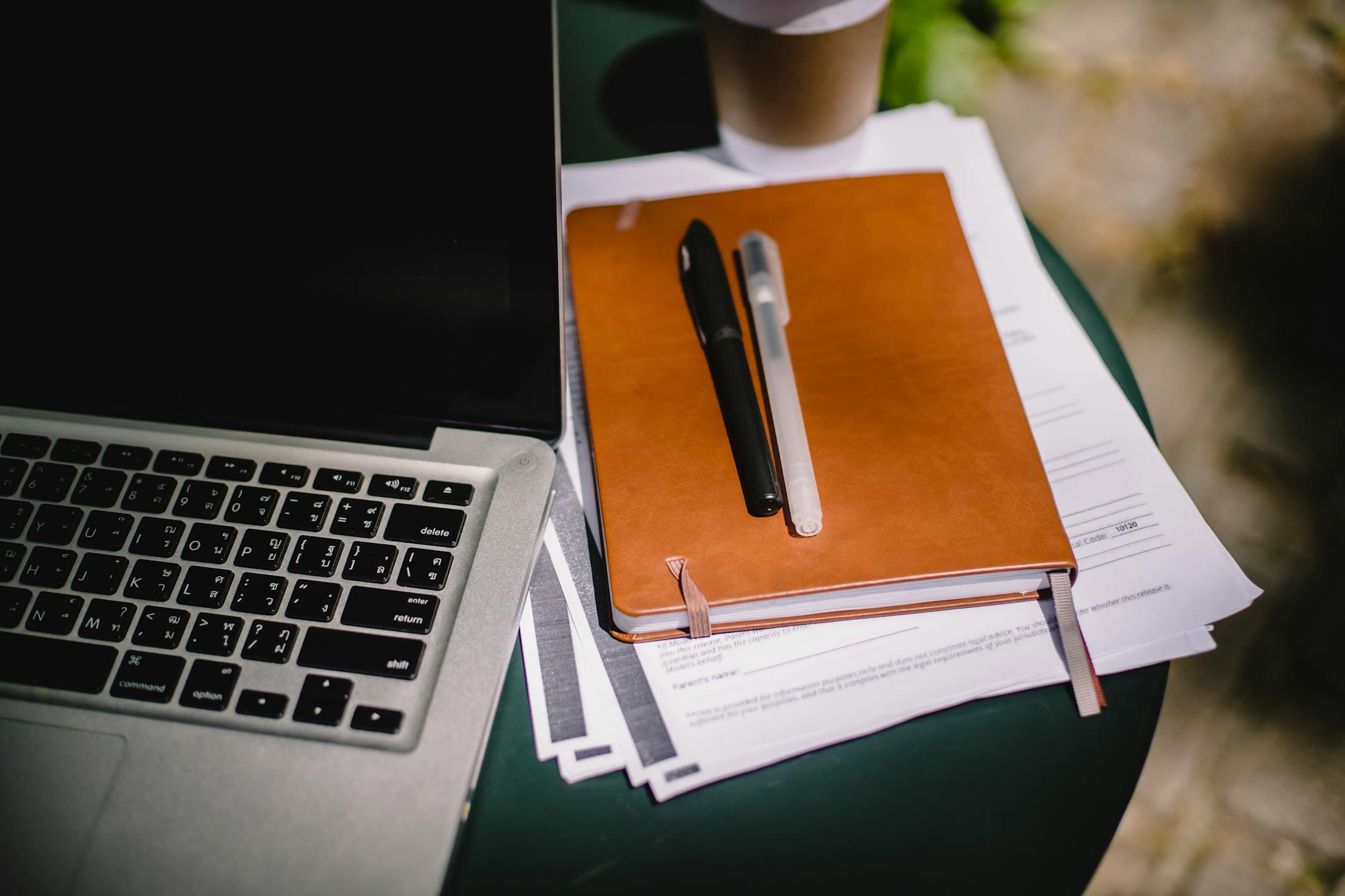 Overhead view of a workspace with a laptop, notebook, and coffee cup on an outdoor table.