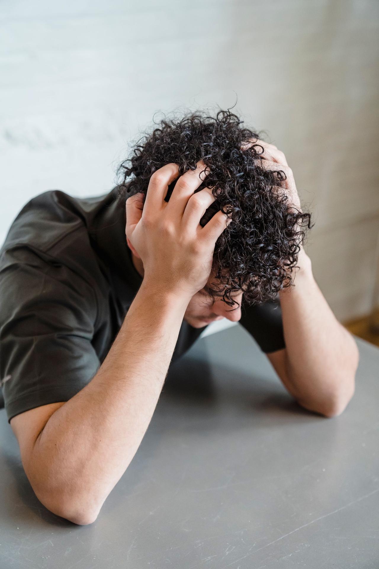 An adult with curly hair looks frustrated, holding head in hands.