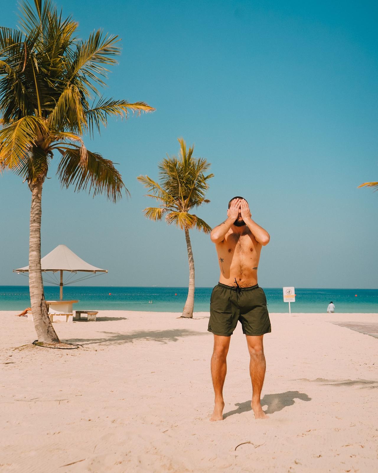 Man on a sunny tropical beach under palm trees, embracing summer vacation vibes.