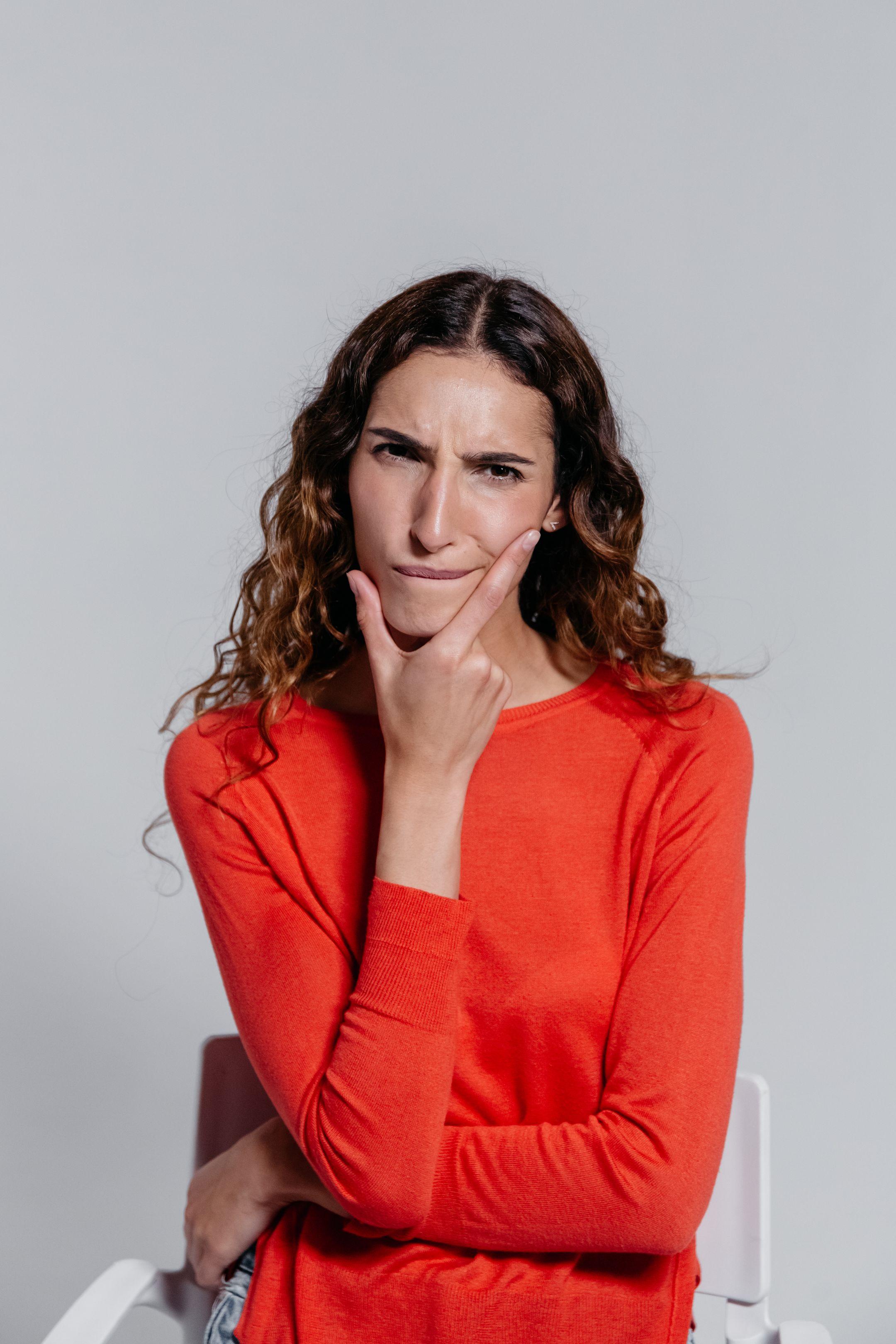 A woman in a red sweater with a thoughtful expression poses indoors, reflecting and pondering deeply.