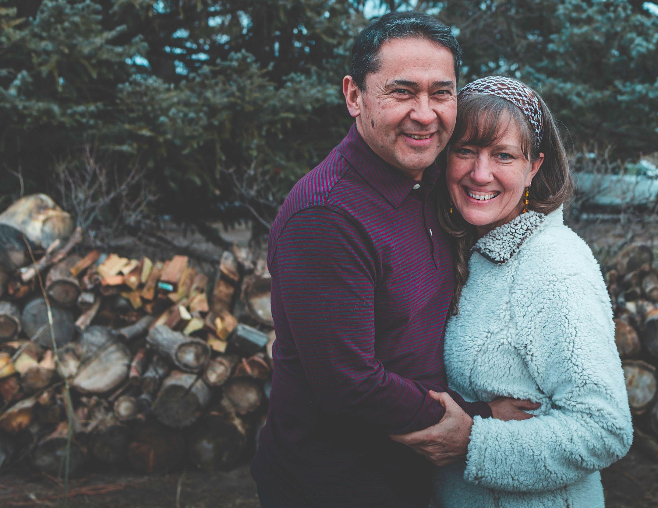 Smiling couple embracing outdoors in winter attire, showcasing happiness and love in a natural setting.
