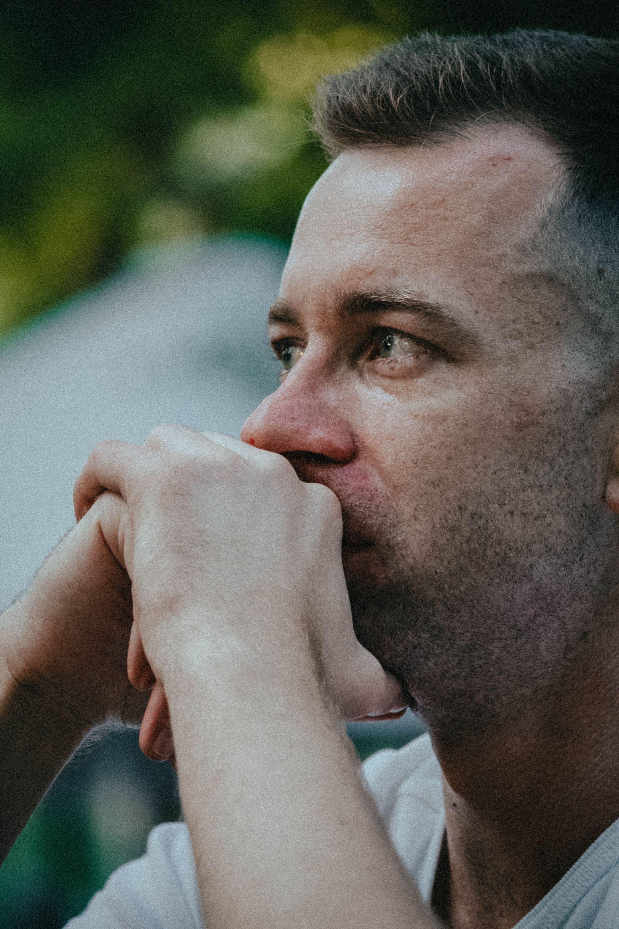 Side profile of a man deep in thought, hands clasped, outdoors.