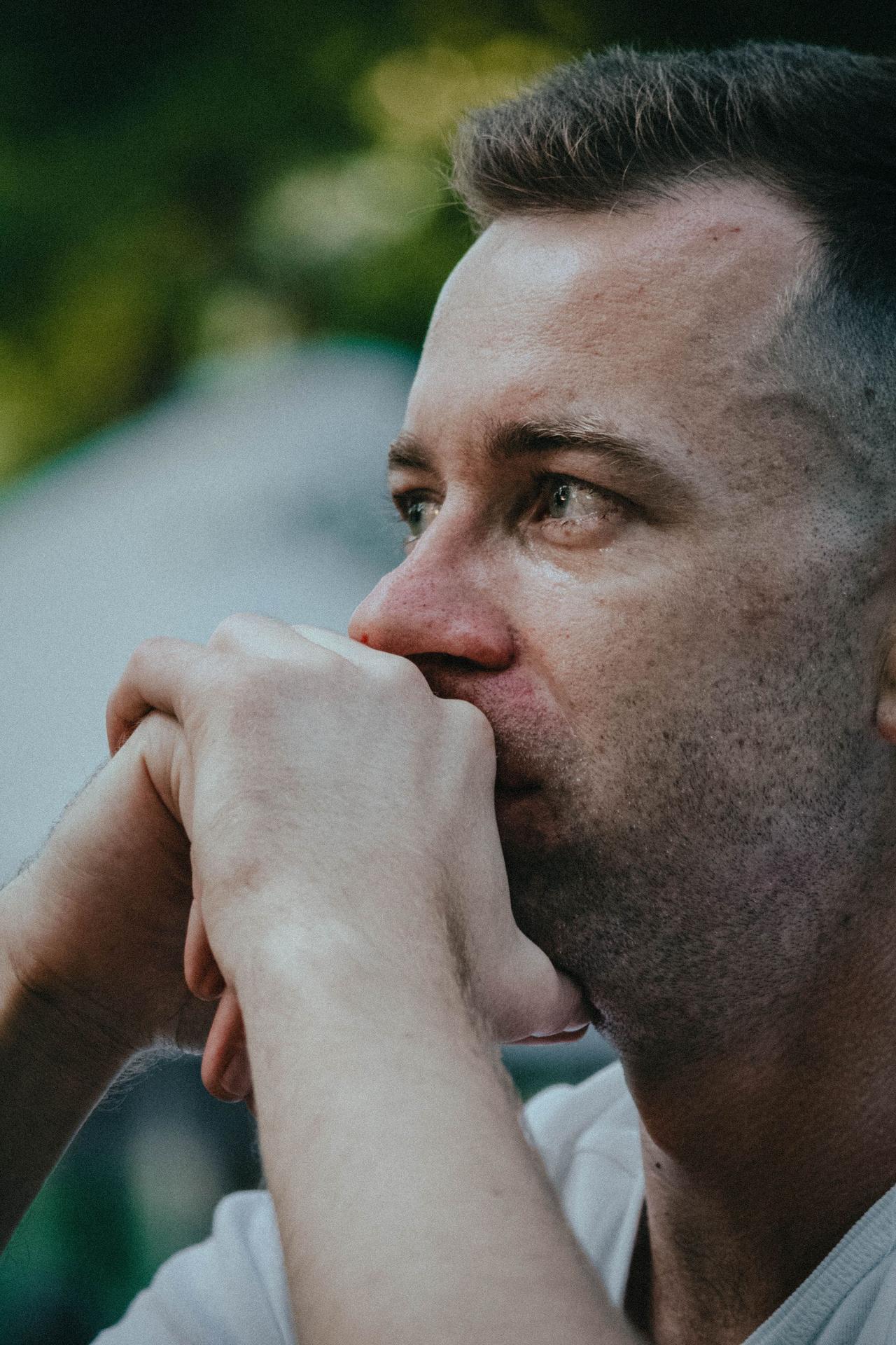 Side profile of a man deep in thought, hands clasped, outdoors.
