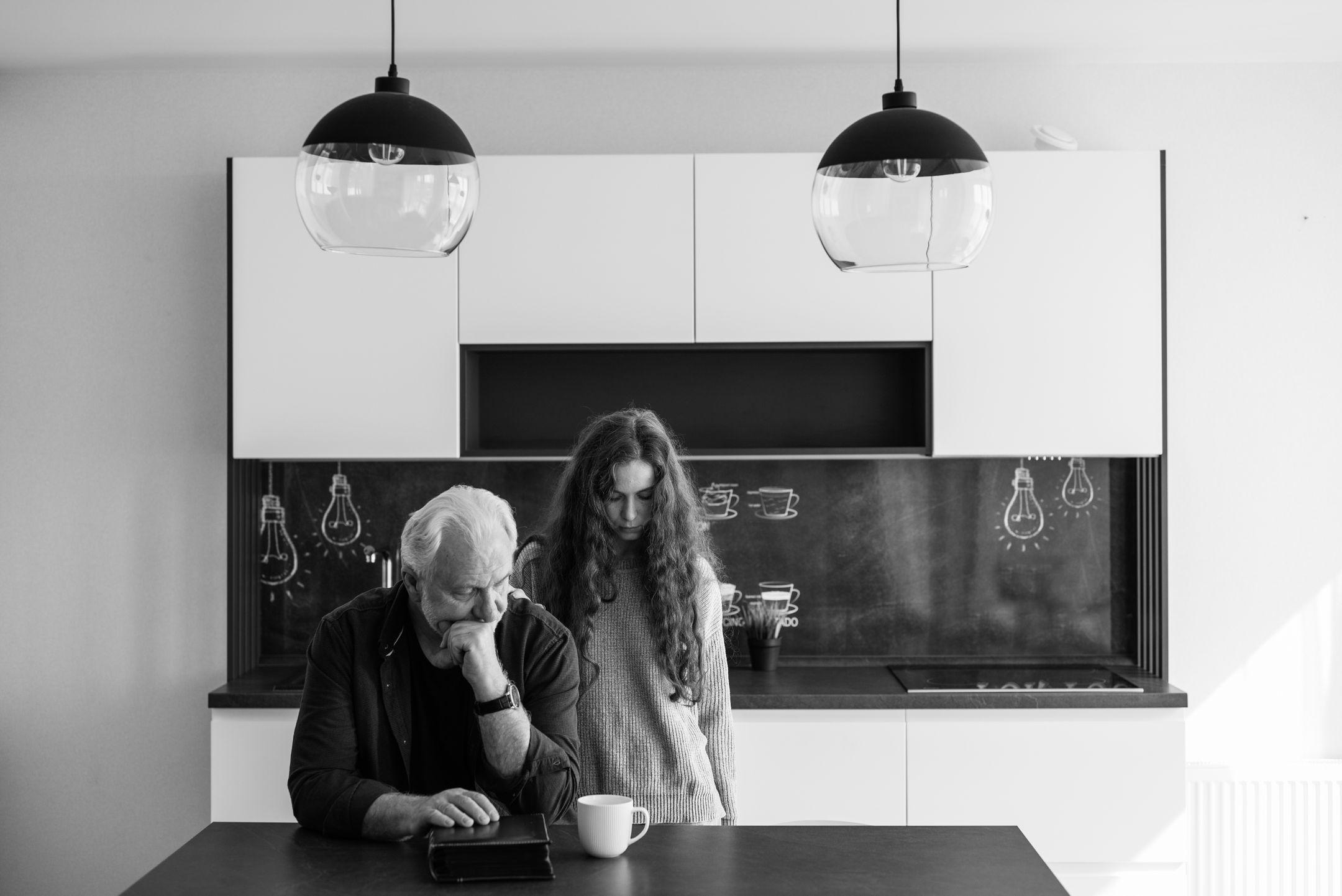 A father and daughter sharing a pensive moment in a modern kitchen setting.