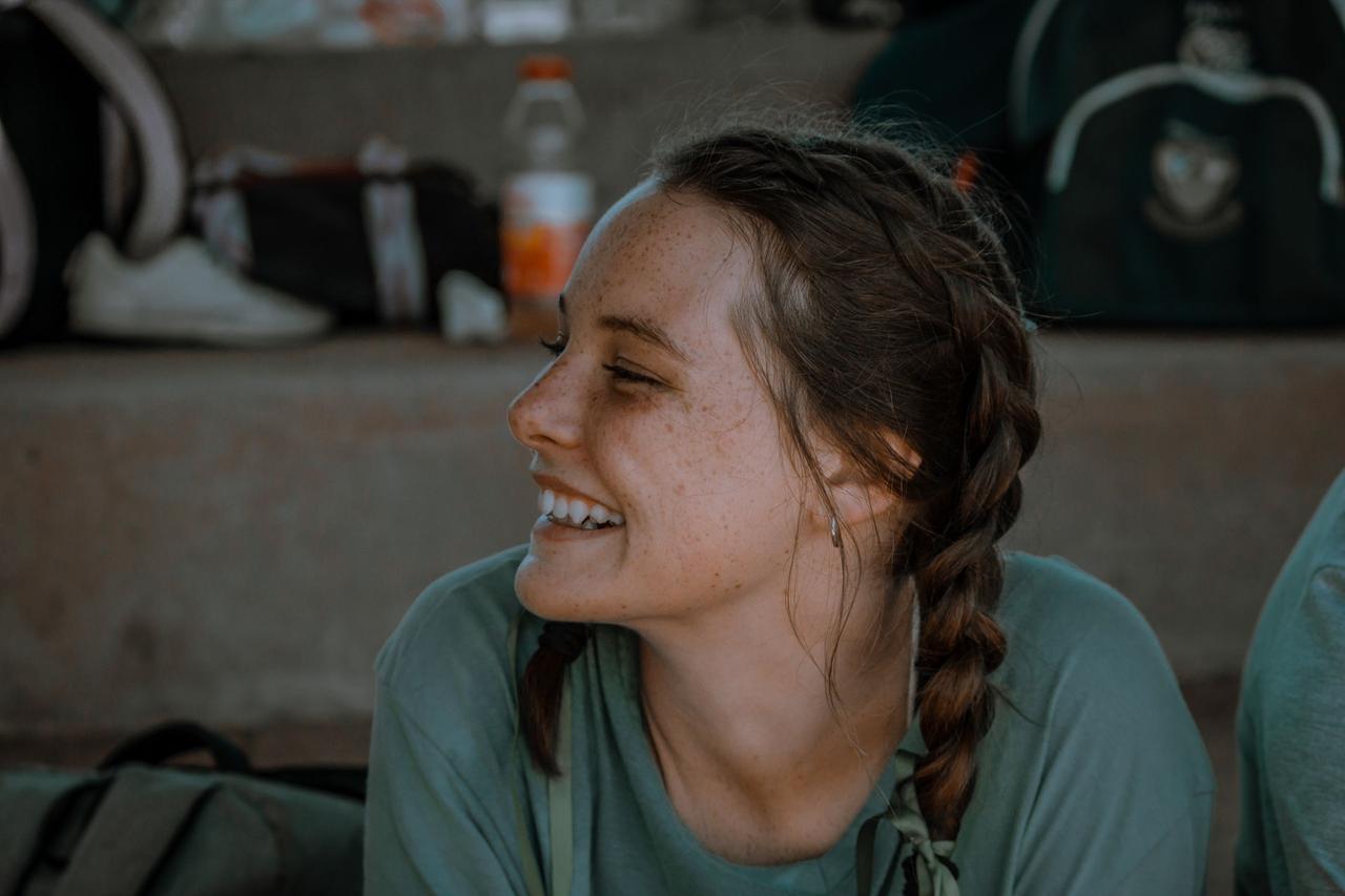 A joyful woman with braided hair smiling, showcasing her freckles in a candid outdoor portrait.