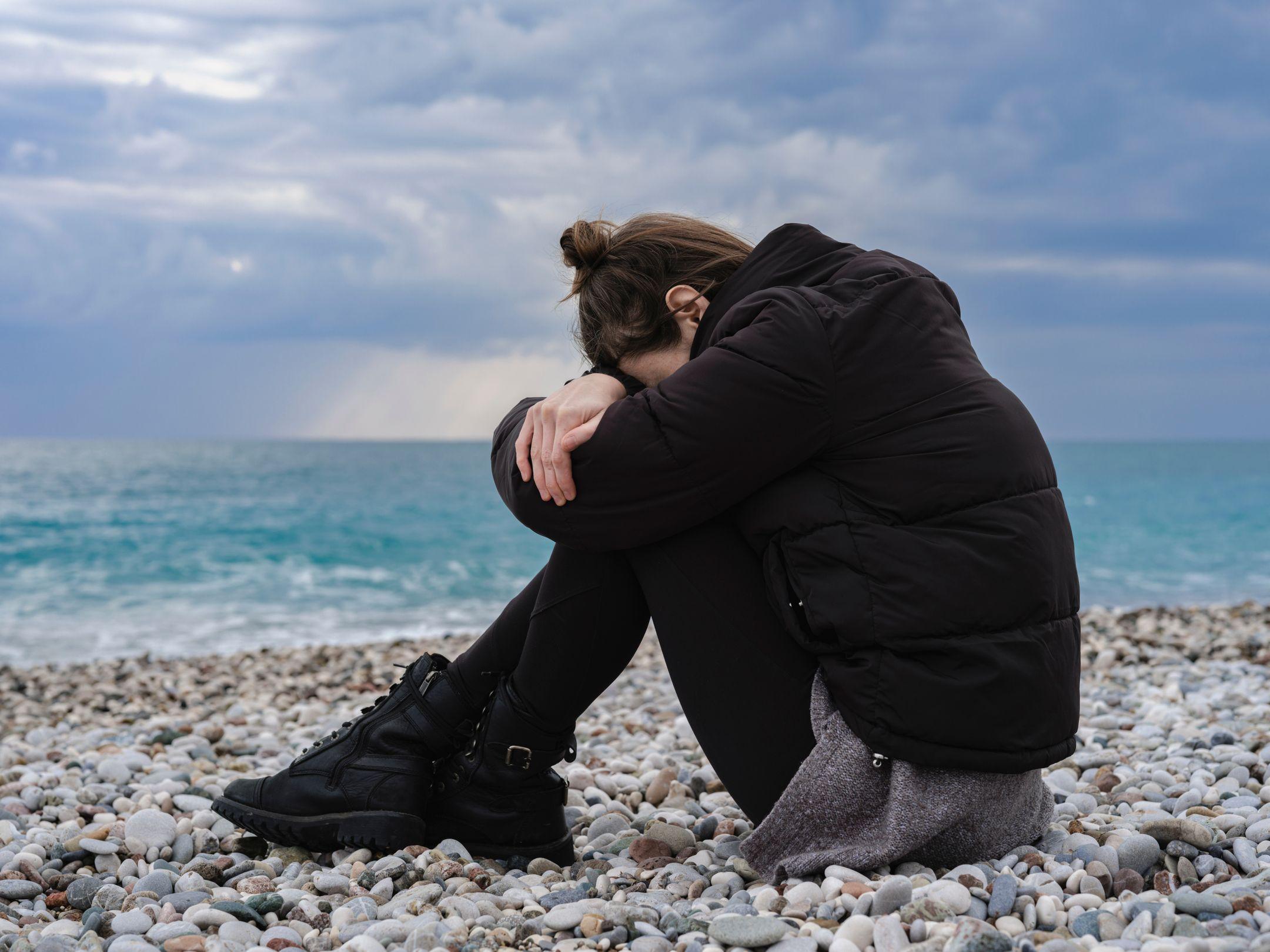 A woman sitting on a rocky beach, expressing solitude and contemplation by the sea.
