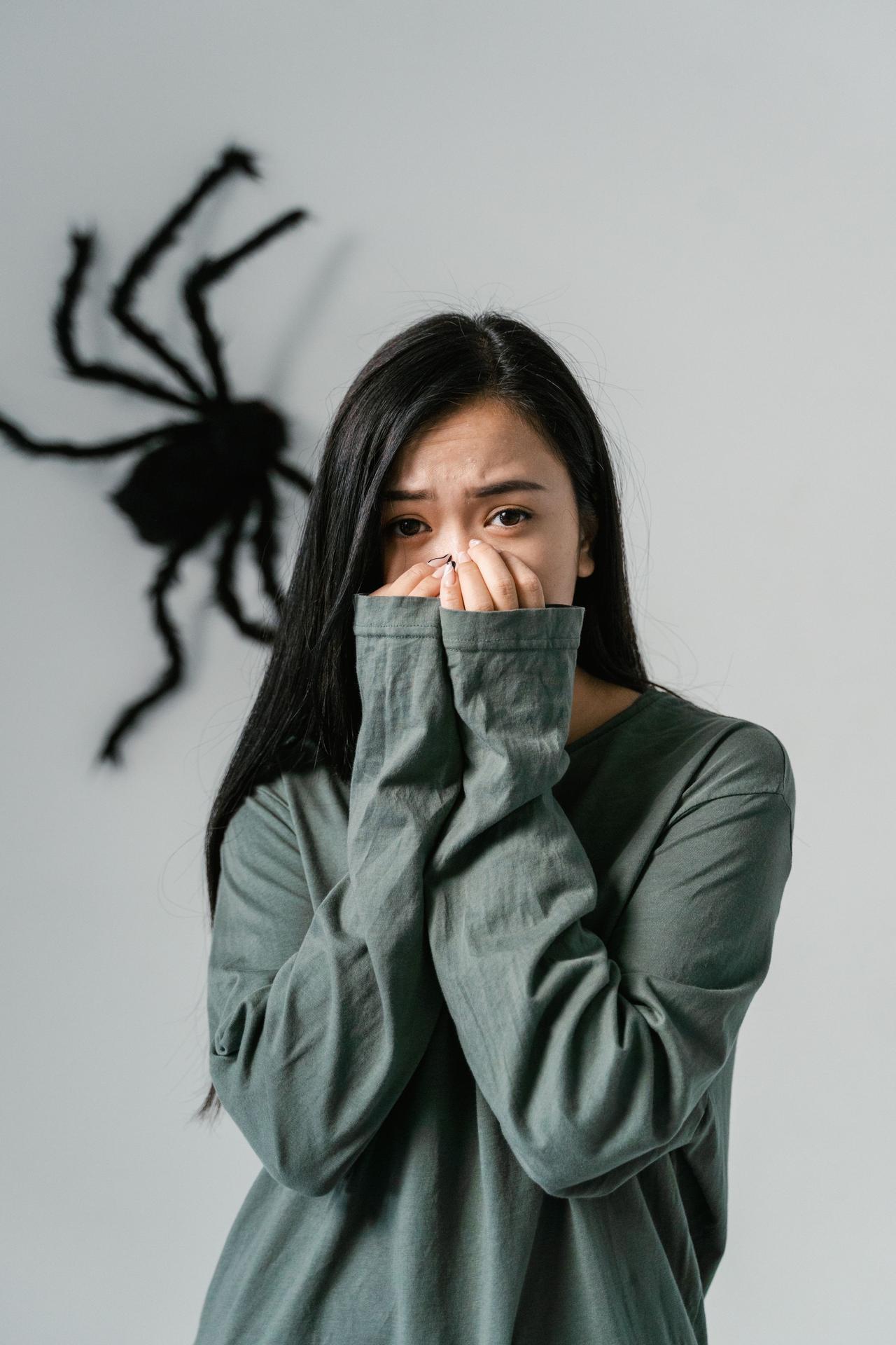 Young woman indoors expressing fear with a spider in the background, capturing an emotional moment.