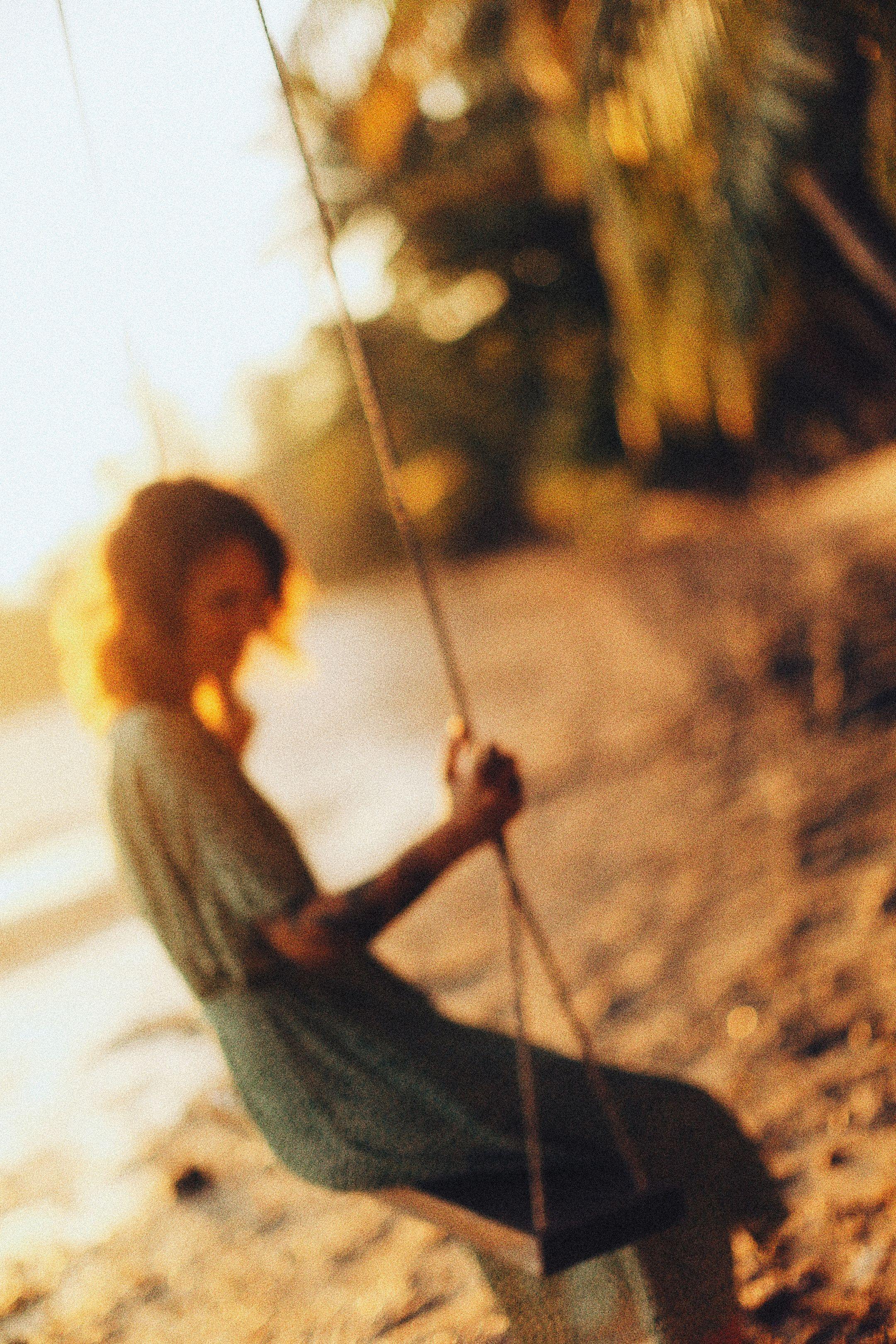 A woman sitting on a swing by the beach during a soft golden sunset, captured with a dreamy focus.