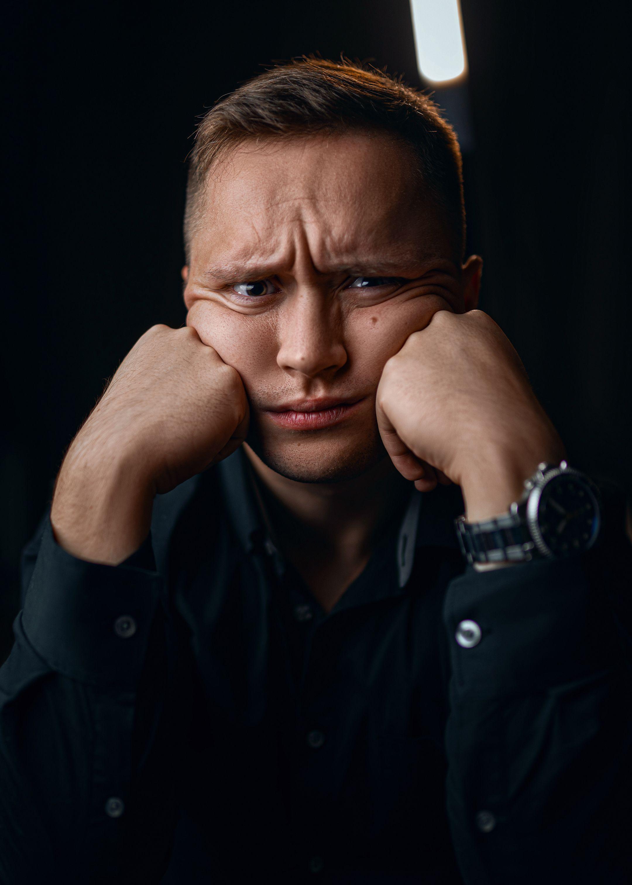 Unhappy male in formal outfit with wristwatch leaning on fists while looking at camera