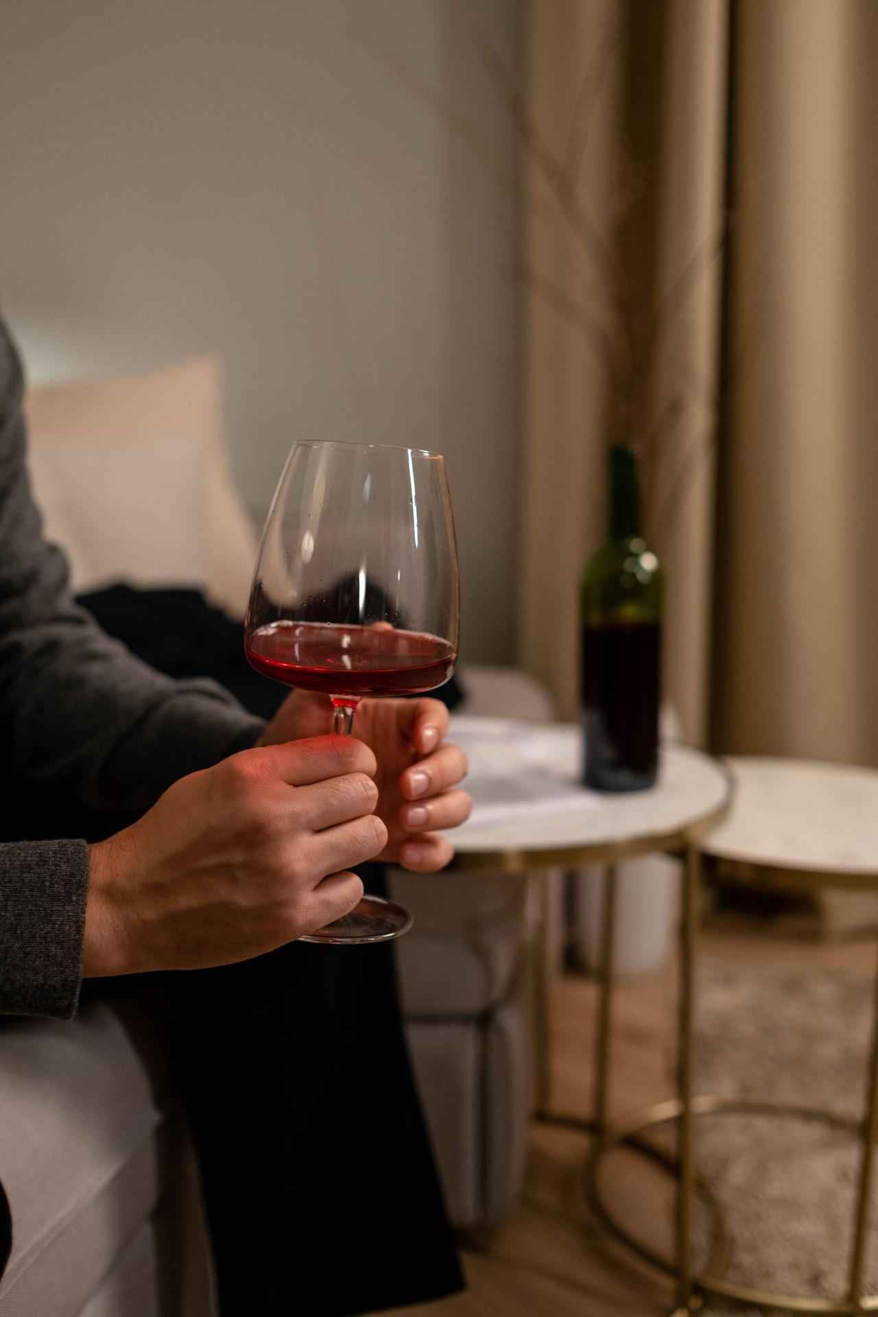 A person holding a red wine glass, capturing a cozy evening ambiance indoors.