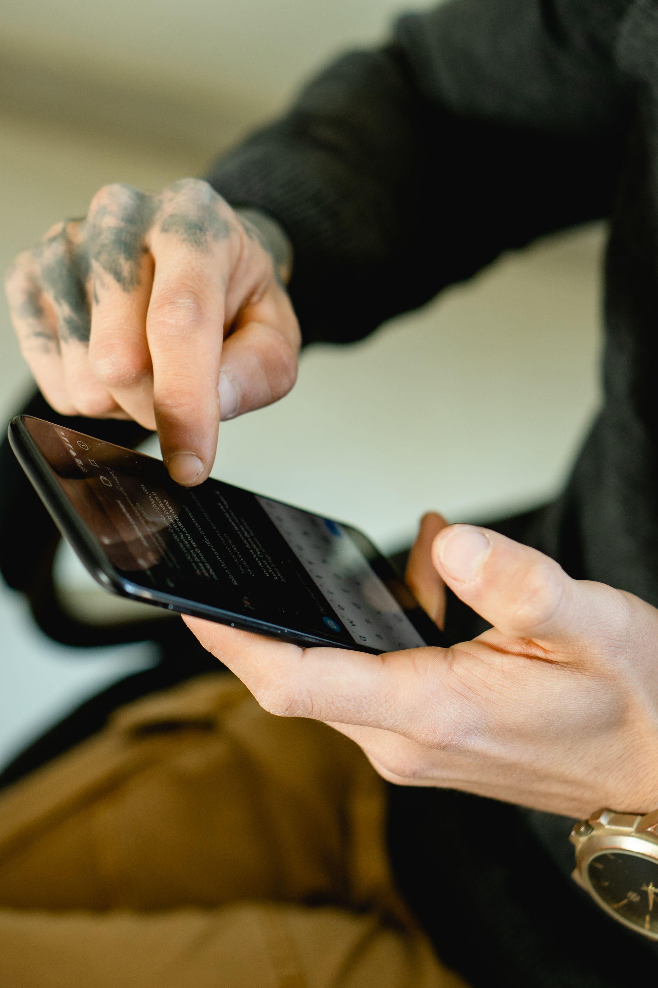 Close-up of tattooed hand touching smartphone screen indoors.