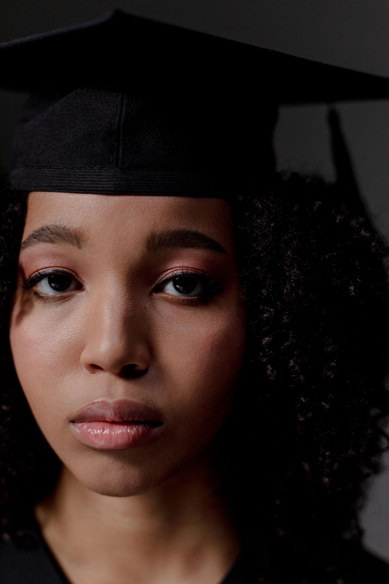 Close-up portrait of a young black female graduate wearing a cap, celebrating her achievement.