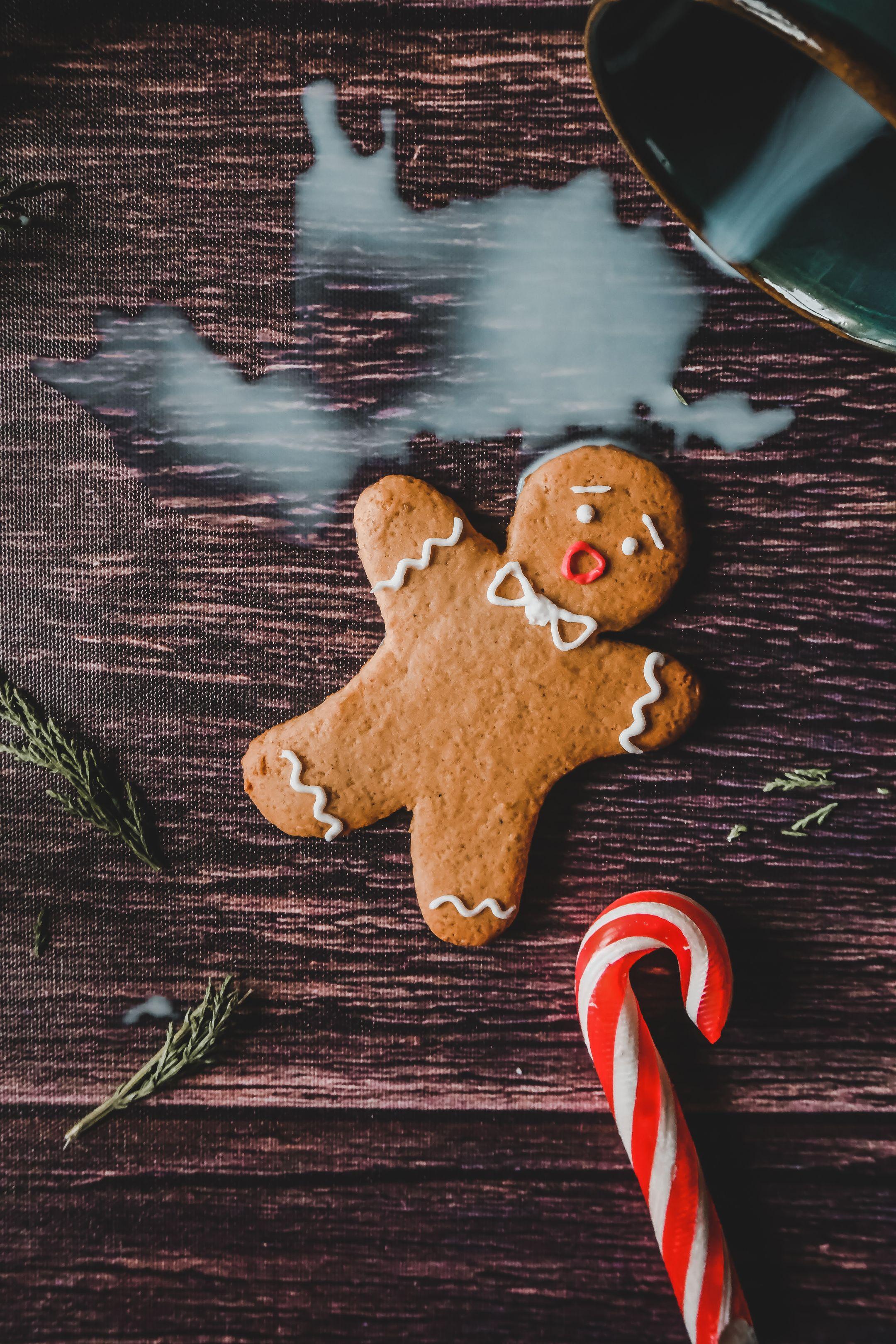 Festive gingerbread cookie with candy cane and spilled milk on wooden surface.