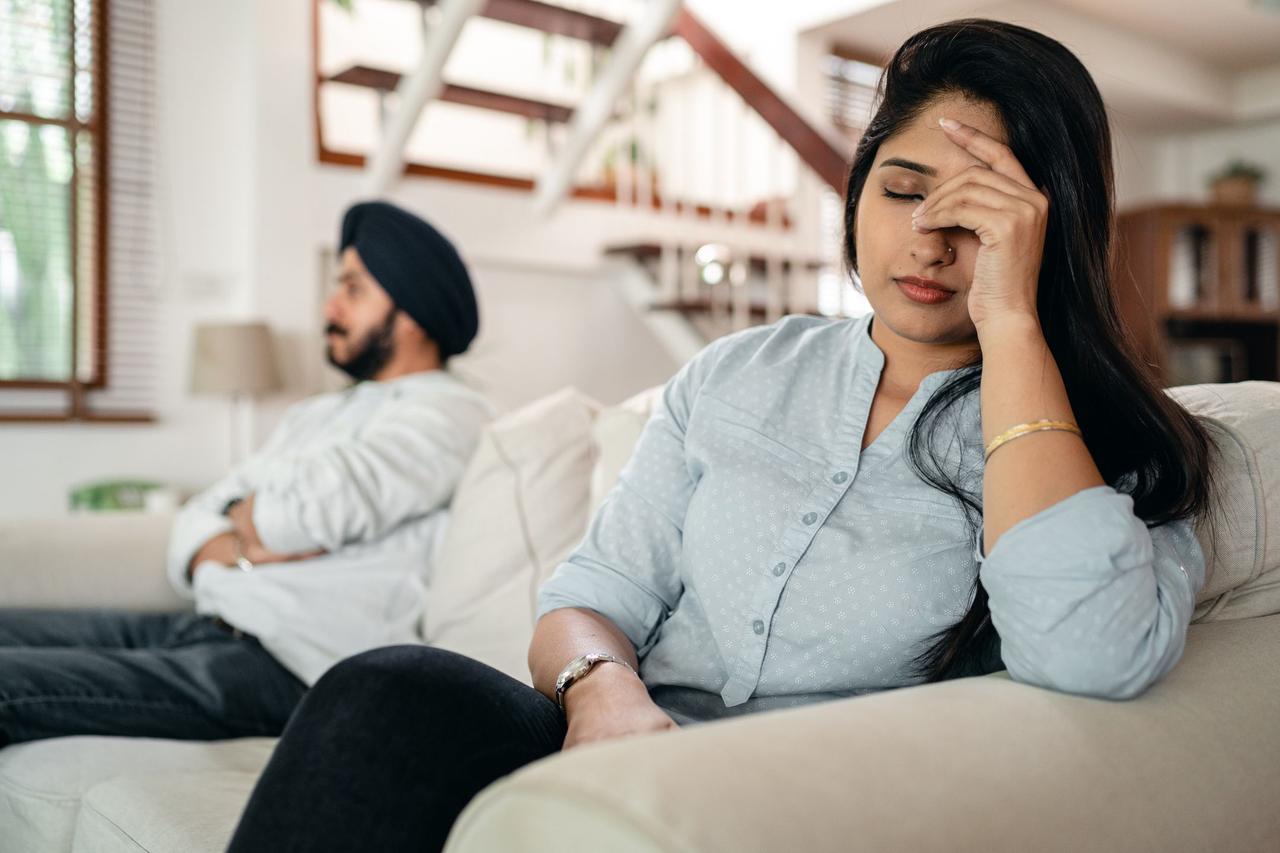 Tired frustrated young Indian woman in casual clothes having headache while sitting on sofa after arguing with husband