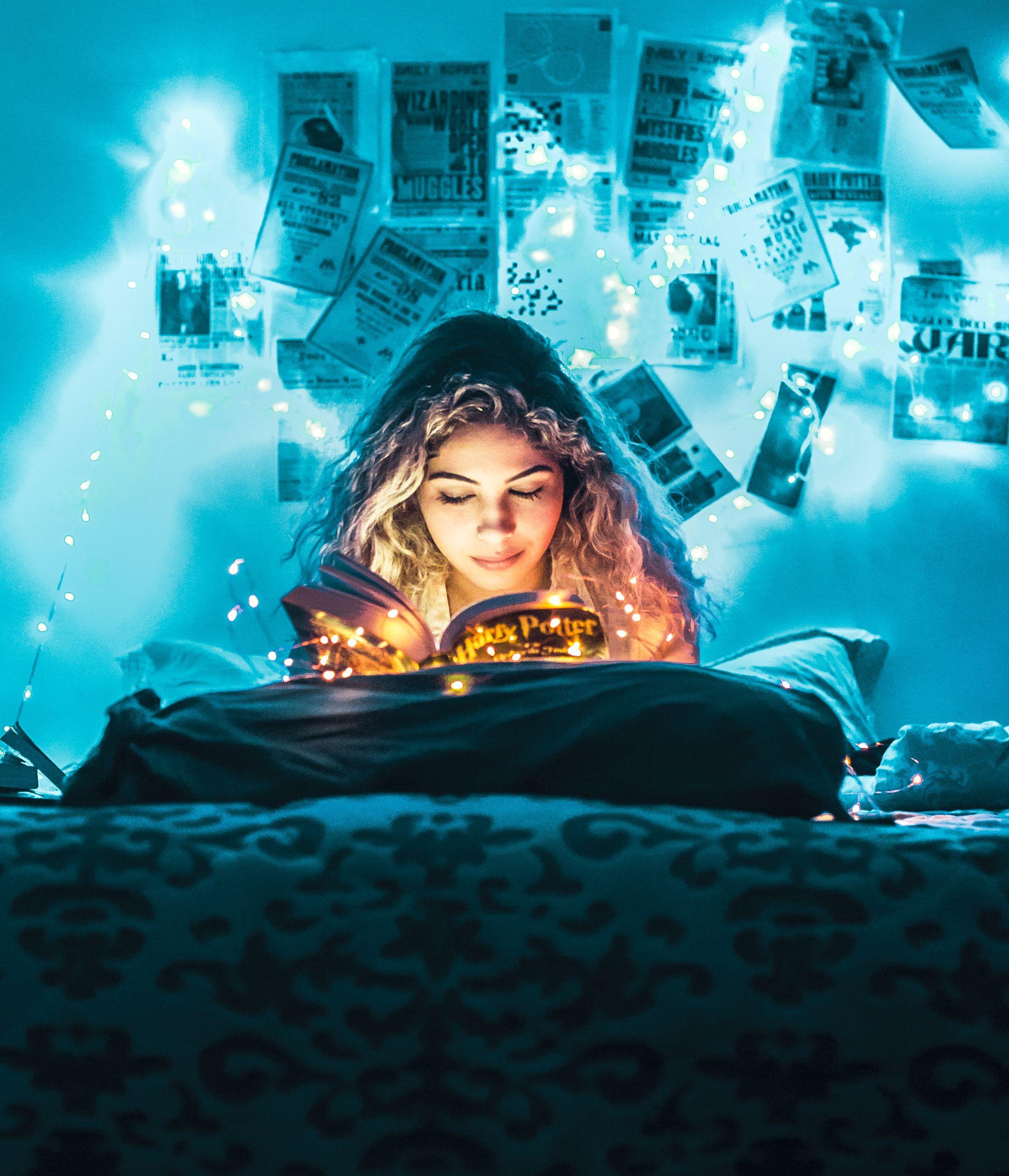 Young woman reading in a cozy bedroom illuminated by magical string lights.