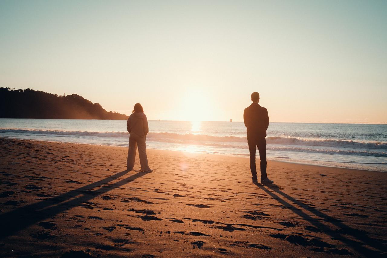 Two people stand on a serene beach, silhouetted against a stunning sunset, capturing a peaceful moment.