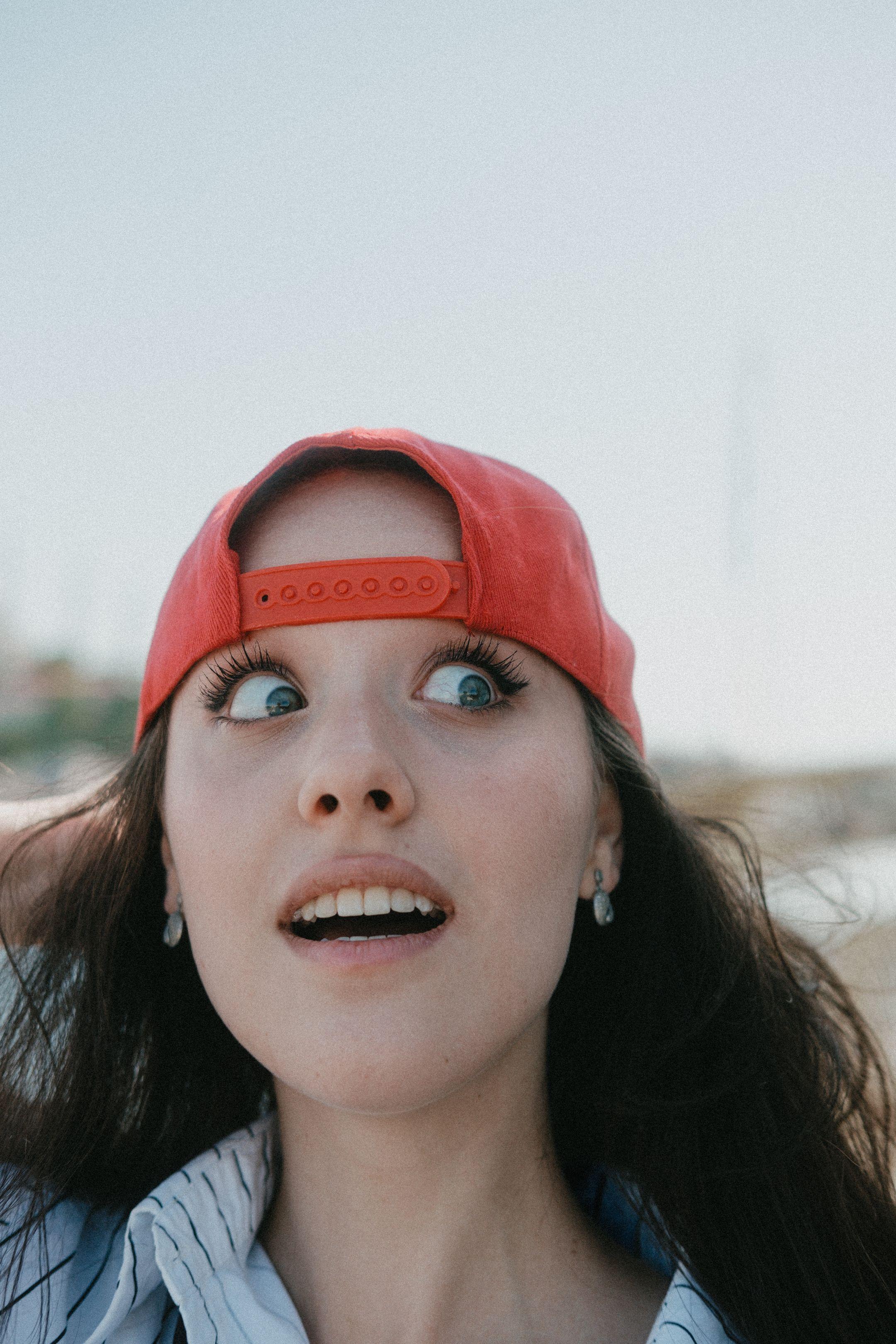 Young woman in red cap looking surprised in an outdoor setting.