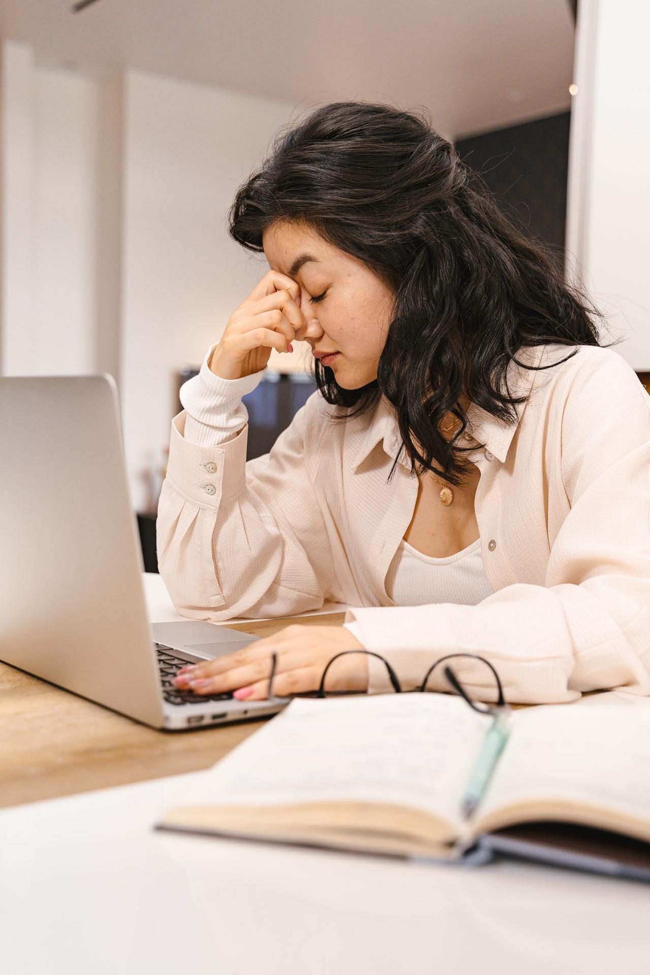 Woman with closed eyes feeling frustration while working on a laptop indoors.