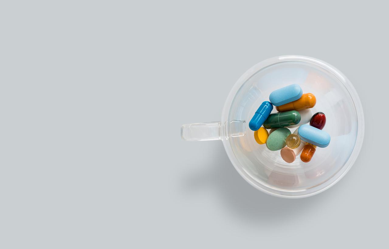 A transparent coffee cup with colourful pills on gray background. Dangerous virus. Virus epidemic concept. Tablets, Medicine and healthy. Close up of capsules. Differend kind of pills. Copy space
