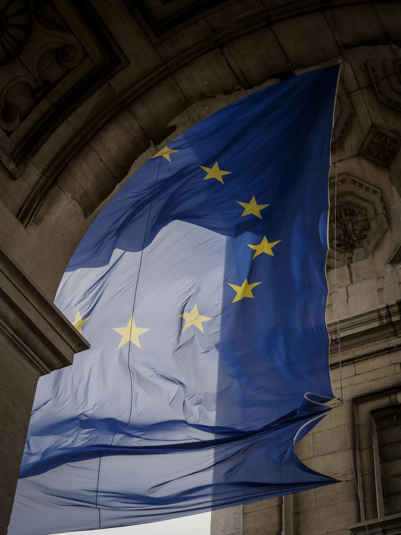 European Union flag waving elegantly within a historic stone archway in Brussels.