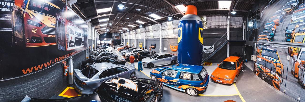 A bustling indoor car meet in Vila Nair, showcasing a range of modified cars and auto enthusiasts.