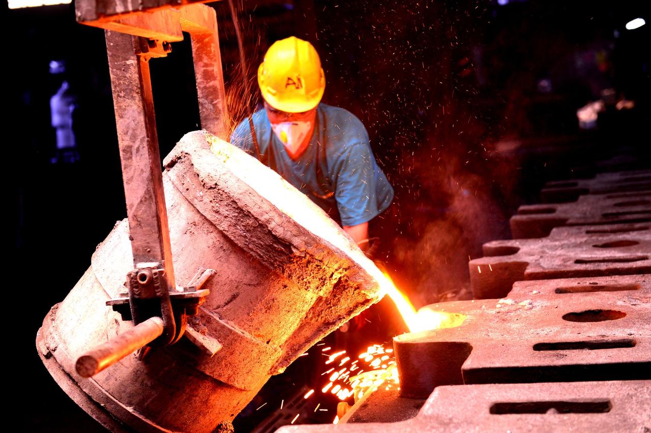 A factory worker wearing a helmet pours molten metal into molds, showcasing industrial metal casting.