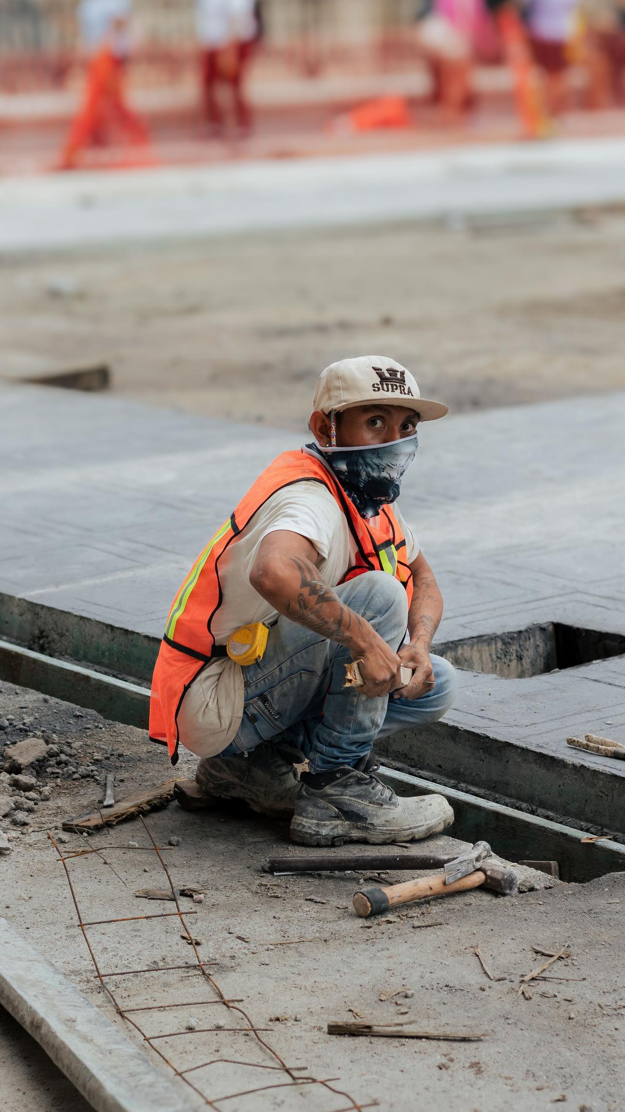 A construction worker in a safety vest is working at an urban site, focused and attentive.