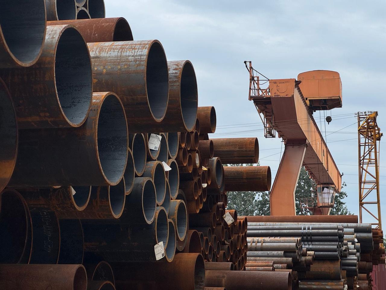 Stacked steel pipes beside an industrial crane in an outdoor yard, showcasing heavy industry and construction materials.