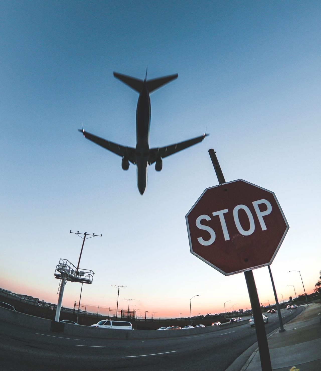 A dramatic shot capturing an airplane flying over a road with a stop sign, silhouetted against the sunset sky.