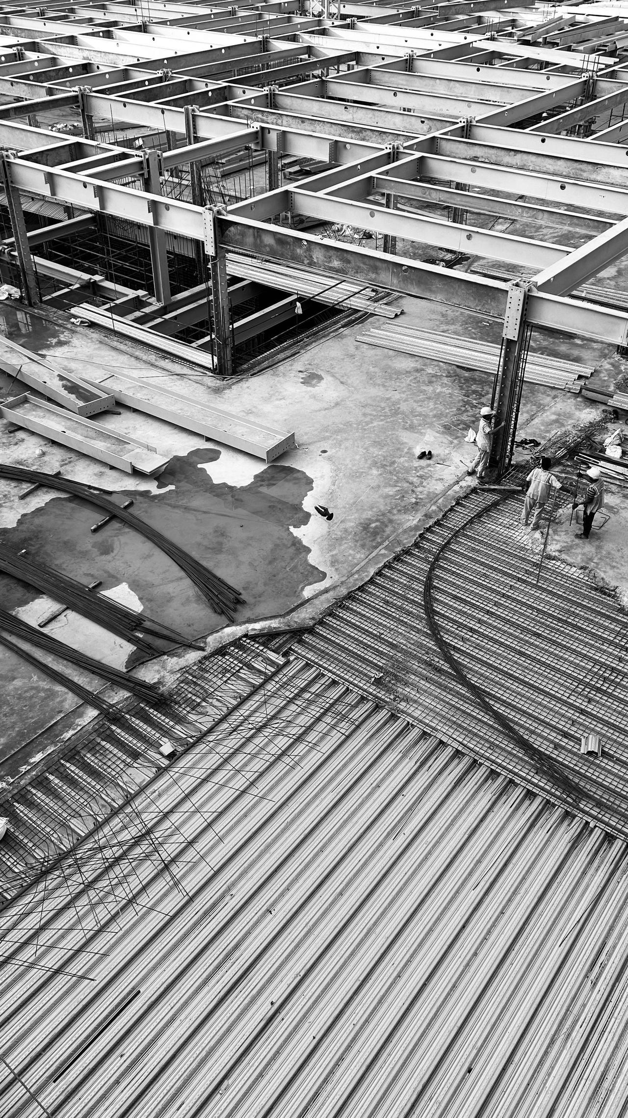 Black and white photo of a construction site with steel framework and workers present.