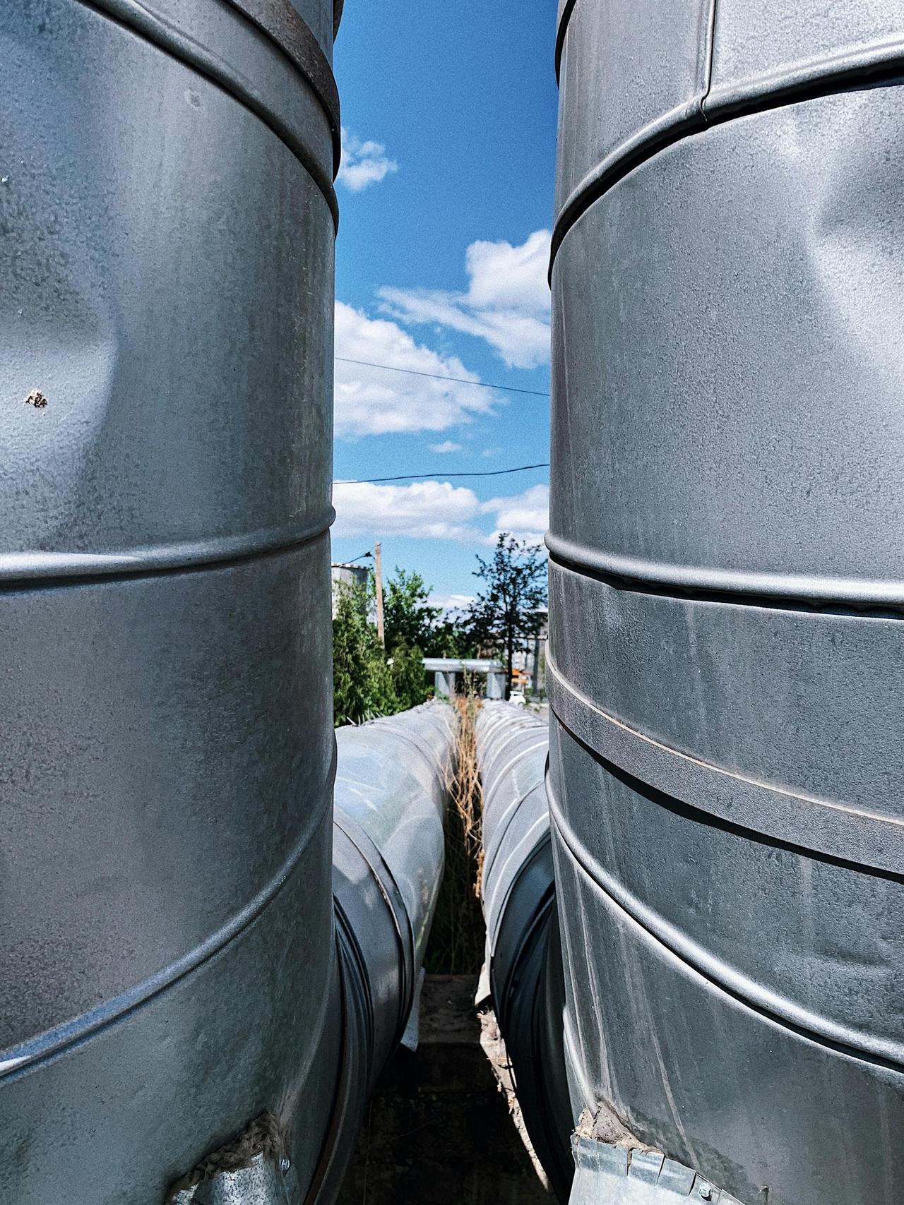 Long iron pipes with dents on ribbed surface representing plumbing system in town under blue cloudy sky in daylight