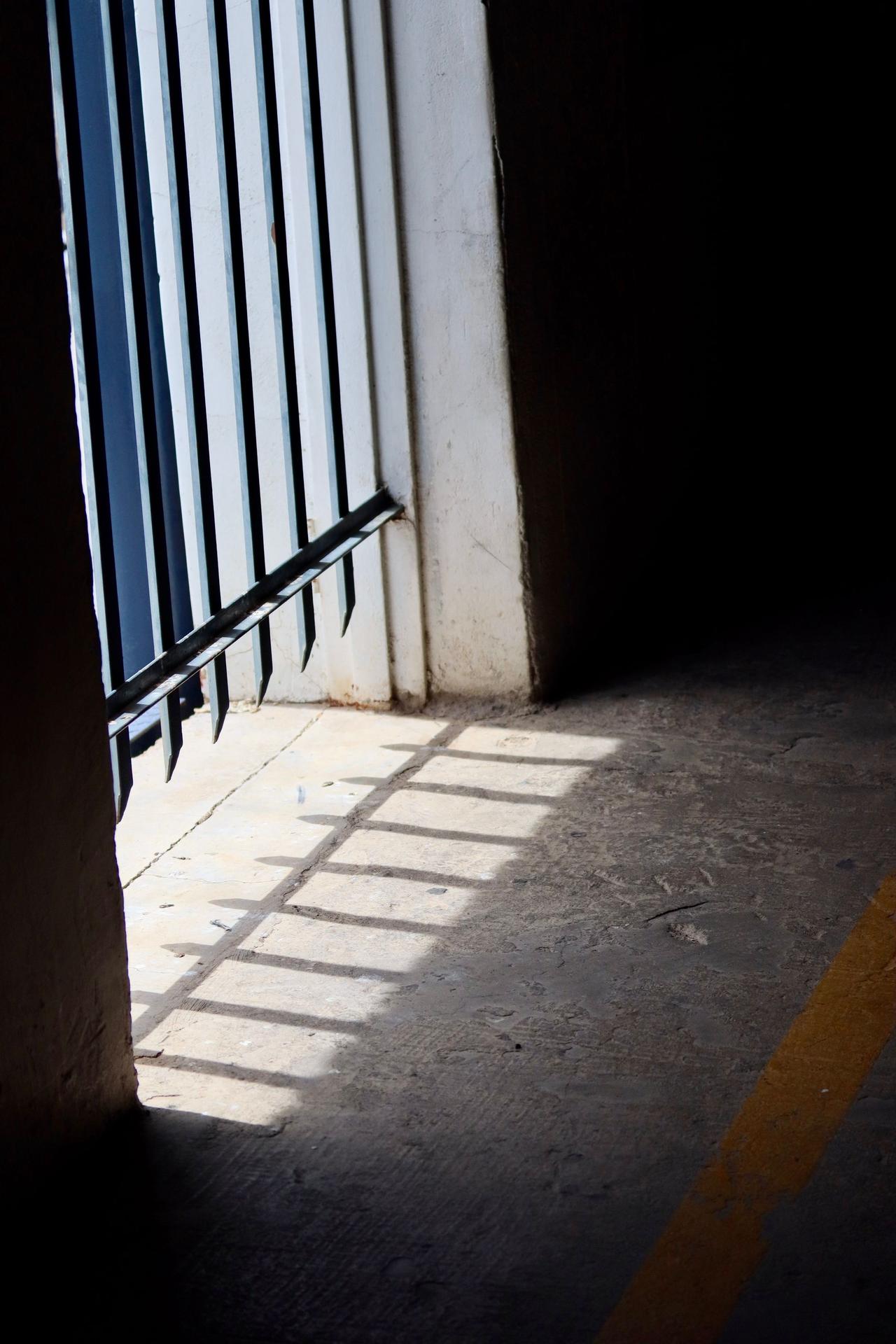 Dramatic shadows cast by sunlight through an open doorway on concrete floor.
