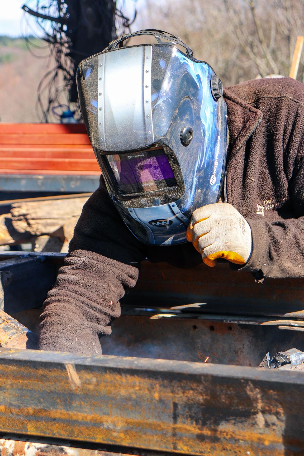 A welder wearing a protective helmet operates in an outdoor setting. Safety and precision.