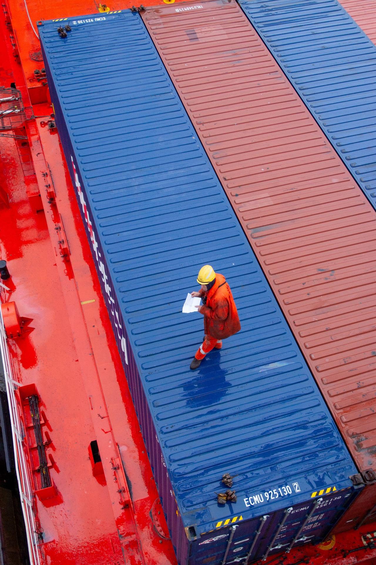 Overhead view of a worker inspecting containers on a ship deck in a maritime setting.