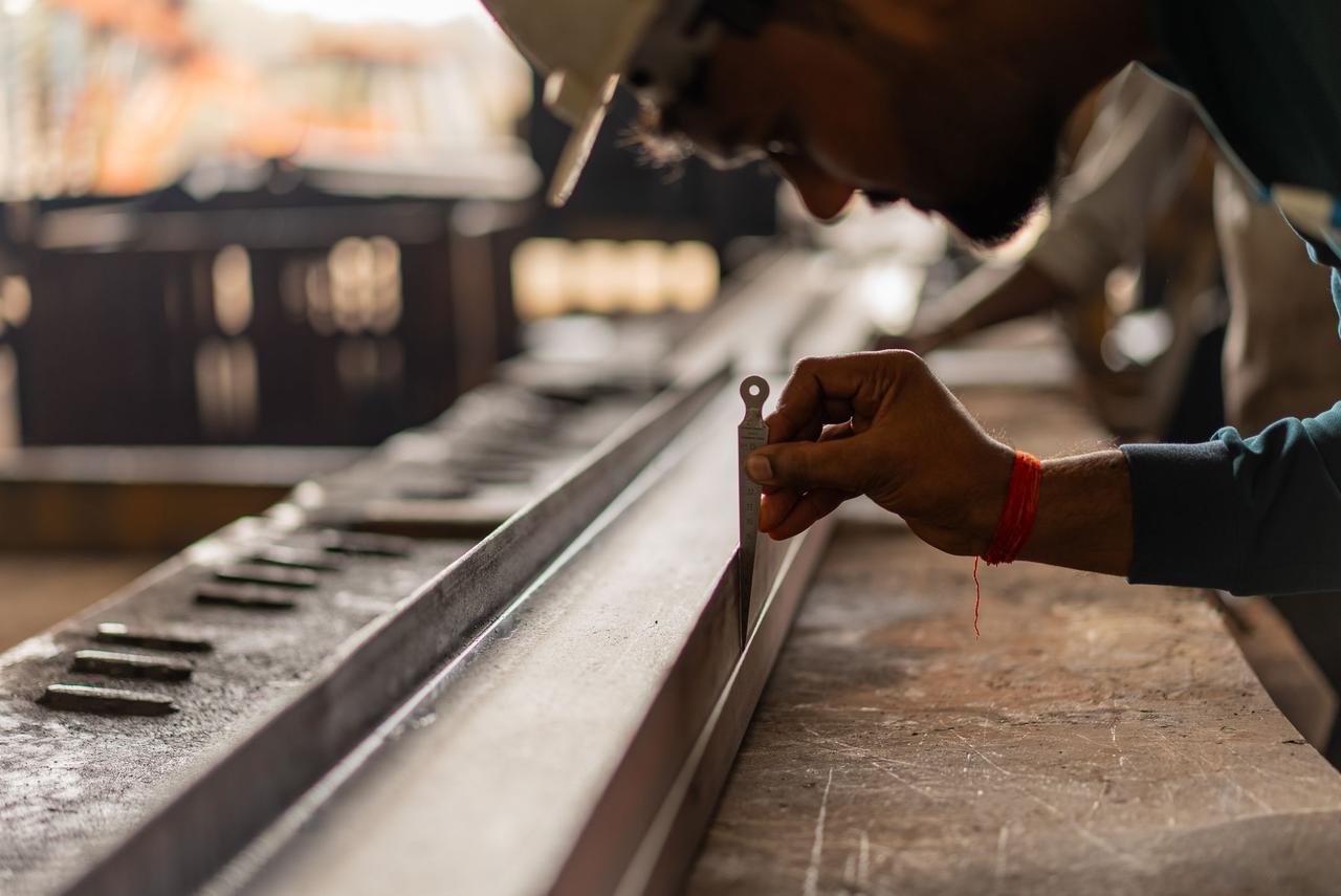 Close-up of a craftsman measuring a metal beam with precision gauge in an industrial workshop setting.