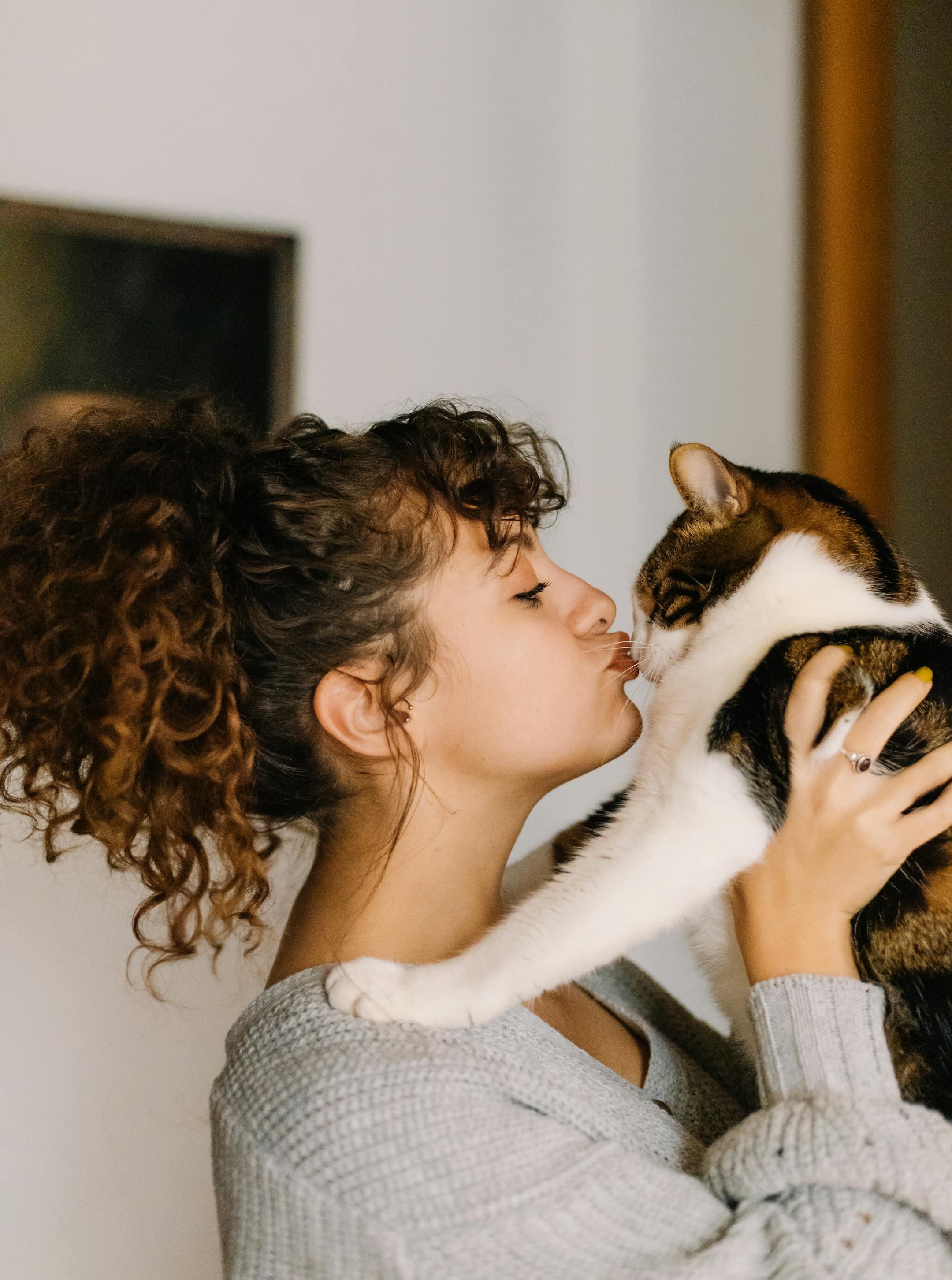 Young woman affectionately kissing her pet cat indoors, capturing a tender moment in İstanbul.