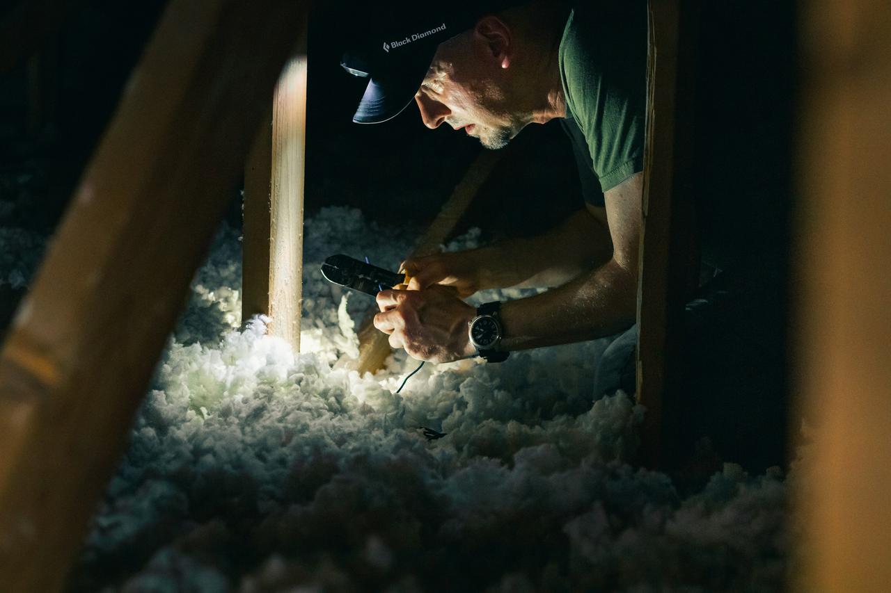man working in dark attic of house with headlamp for light source
