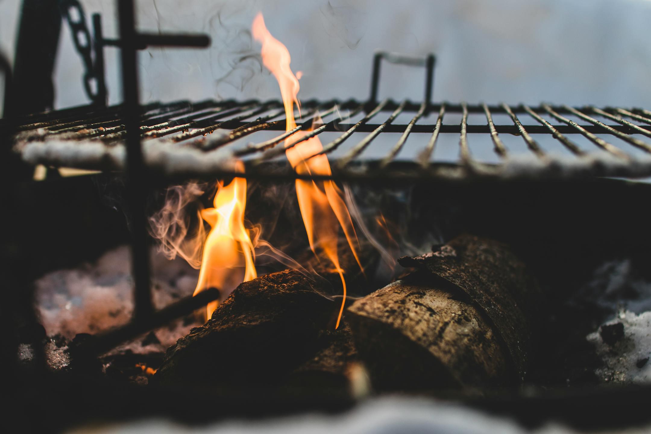Close-up view of firewood burning in a fire pit with a metal grill above, outdoor setting.