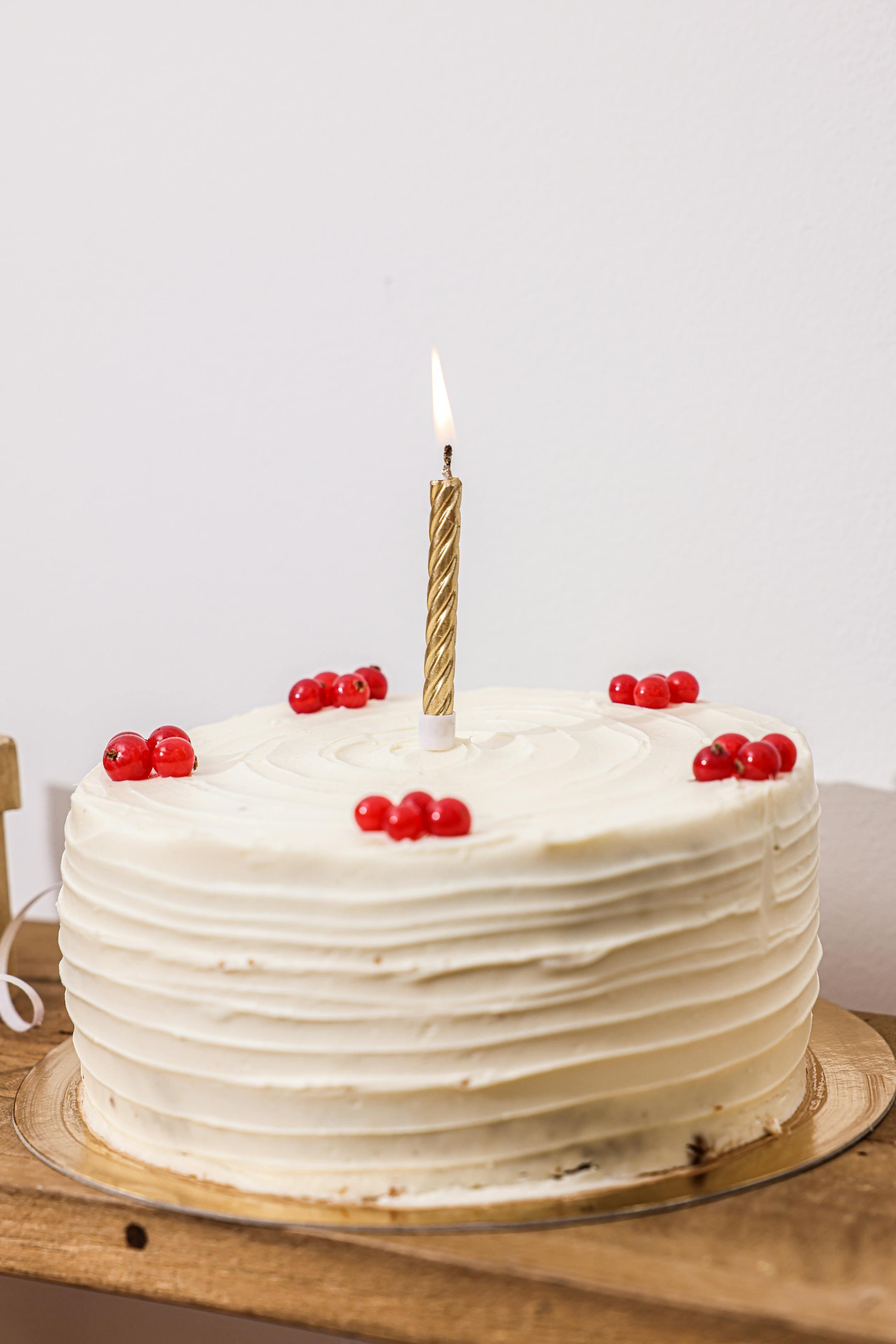 A close-up of a white frosted birthday cake adorned with berries and a single lit candle.