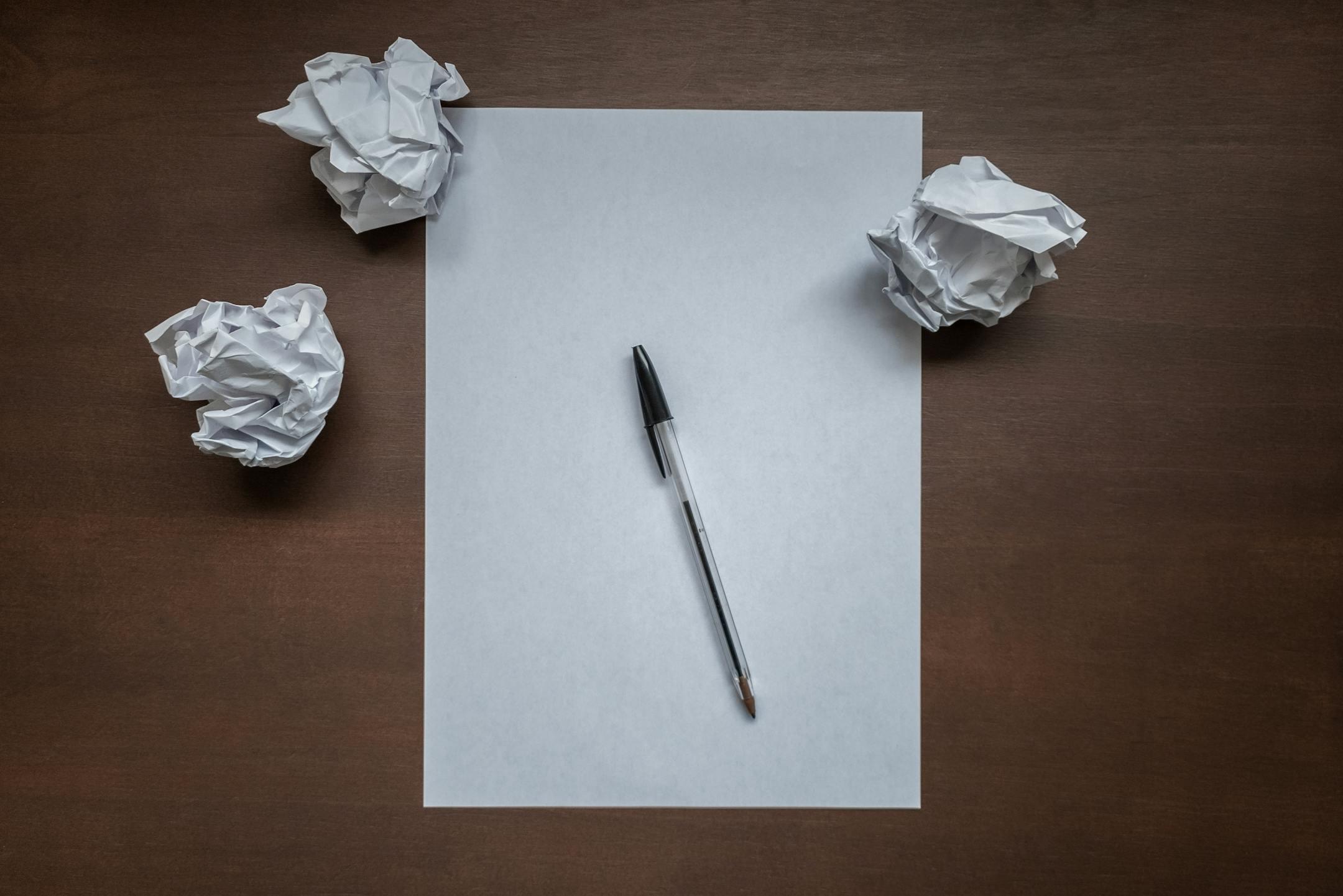 Crumpled paper and pen on desk, symbolizing writer's block or creativity struggles.