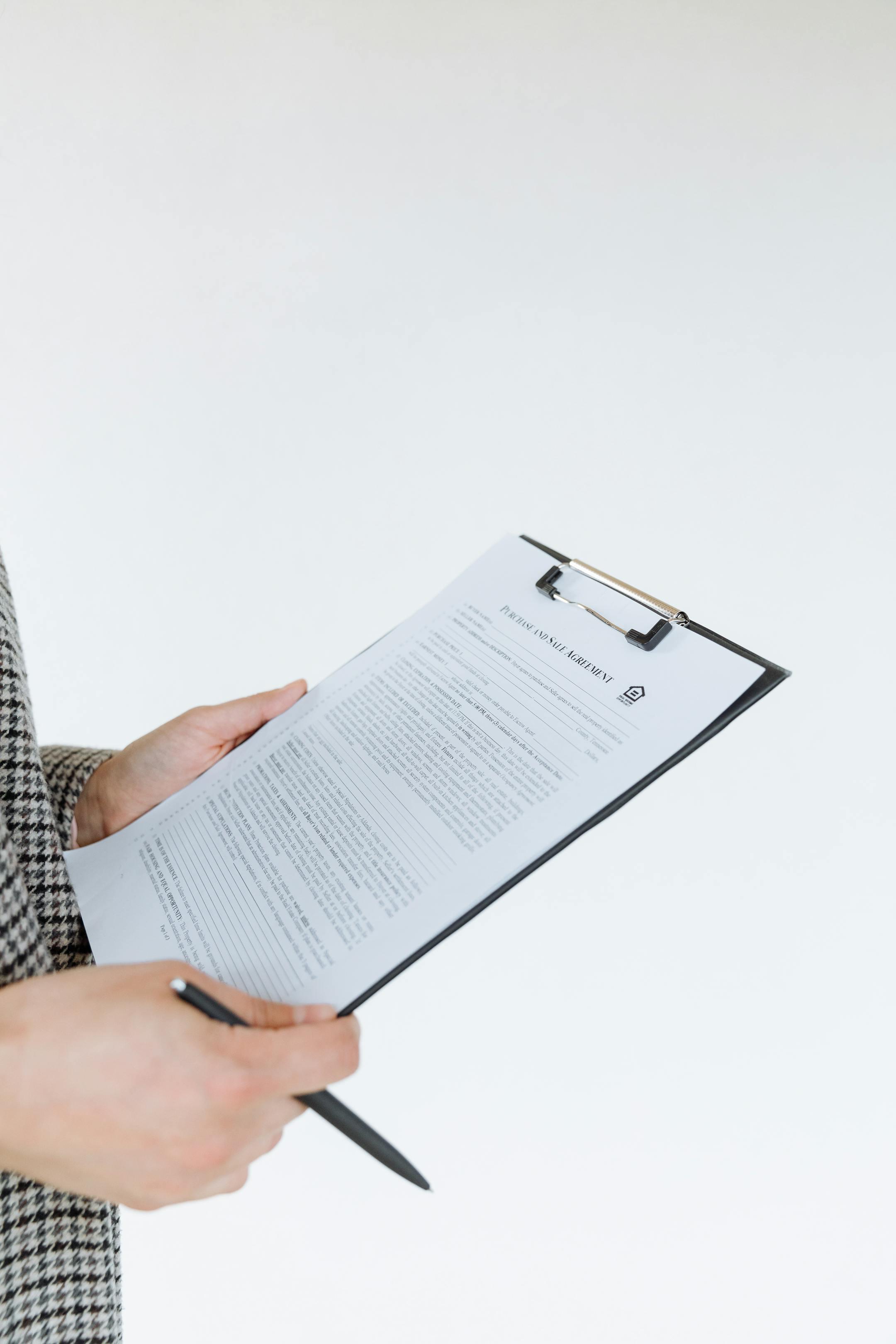 Person holding a filled contract on a clipboard with a pen against a white background.