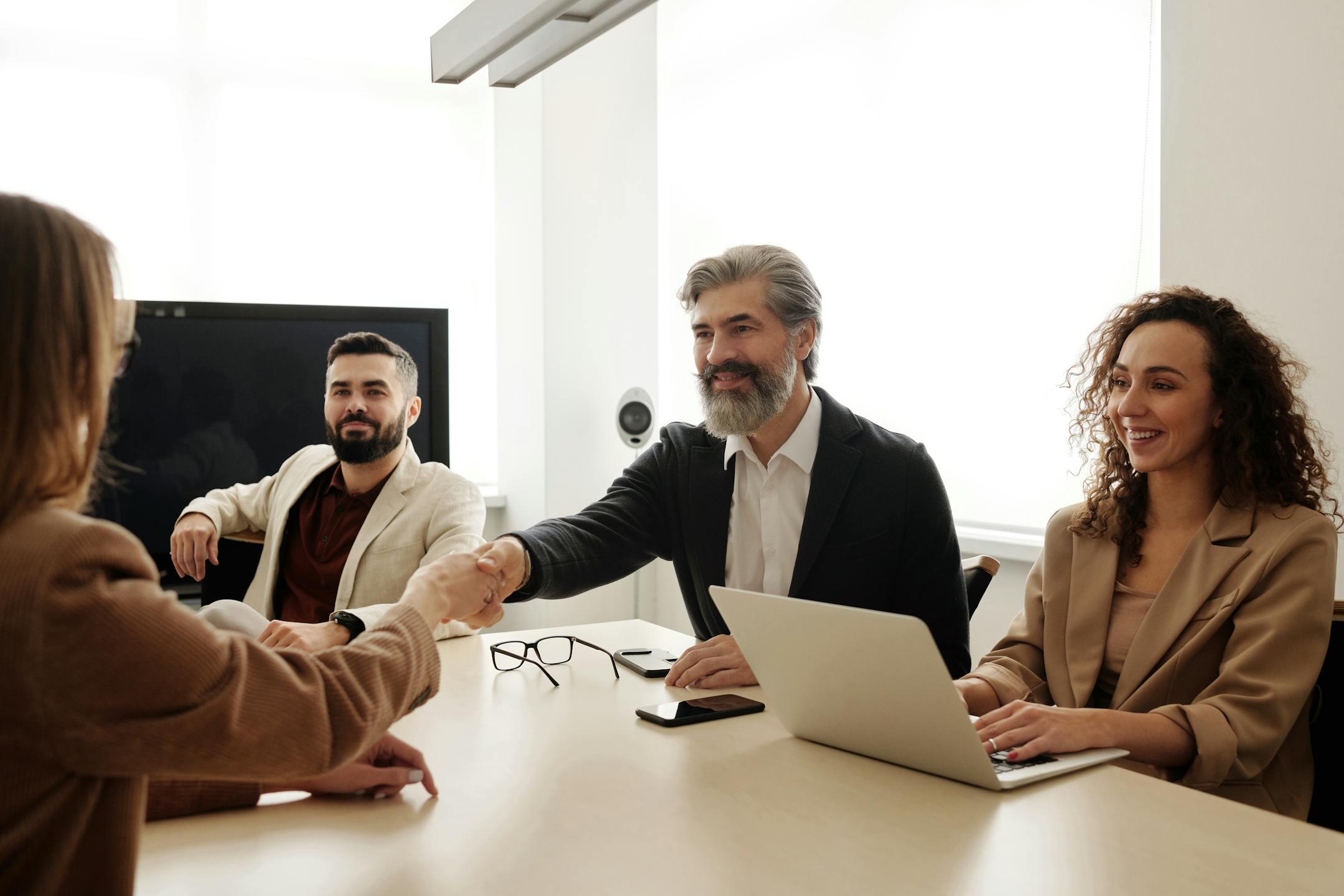 A group of business professionals shake hands during a meeting regarding executive compensation.