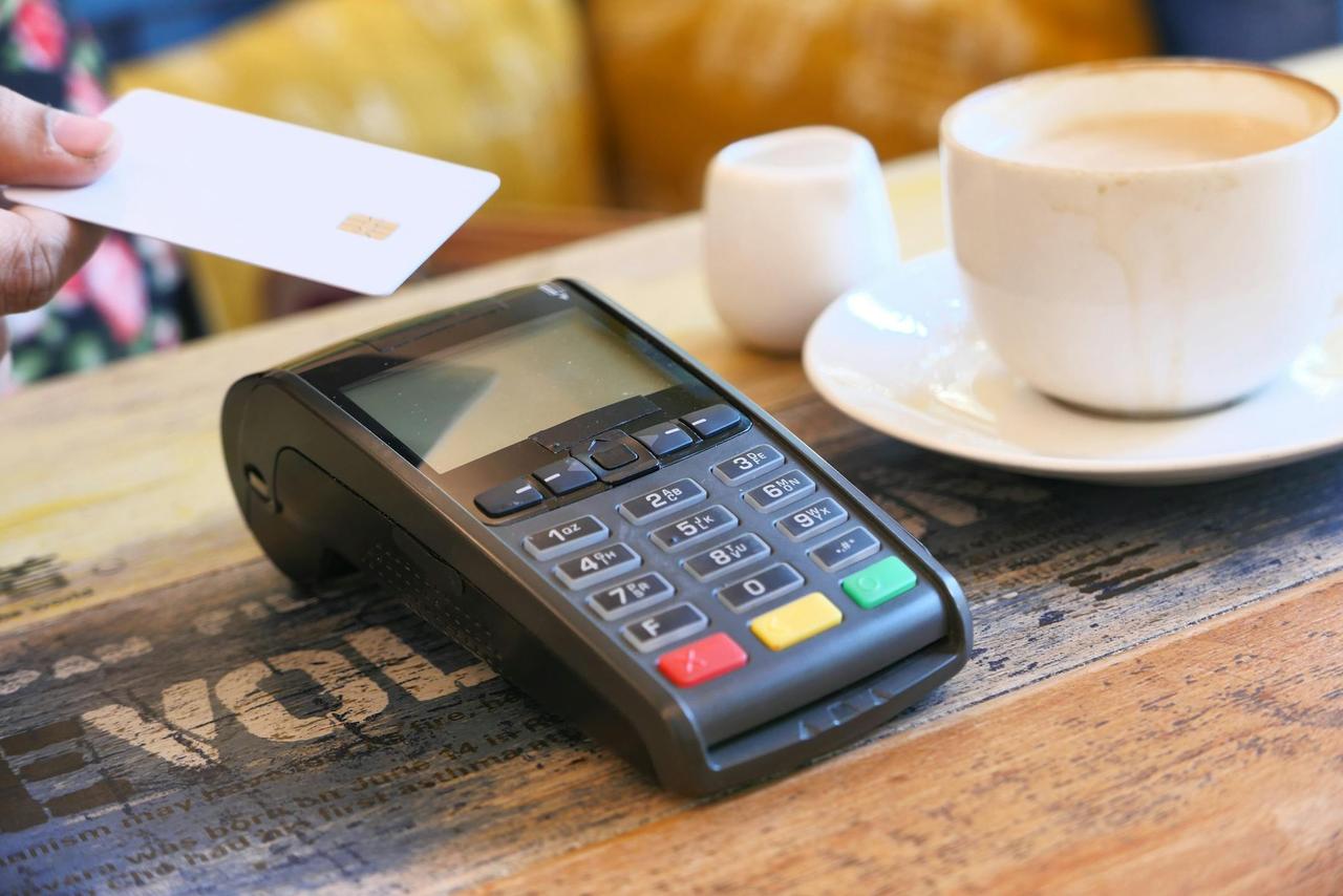 Close-up of contactless payment with credit card on a terminal beside a coffee cup.
