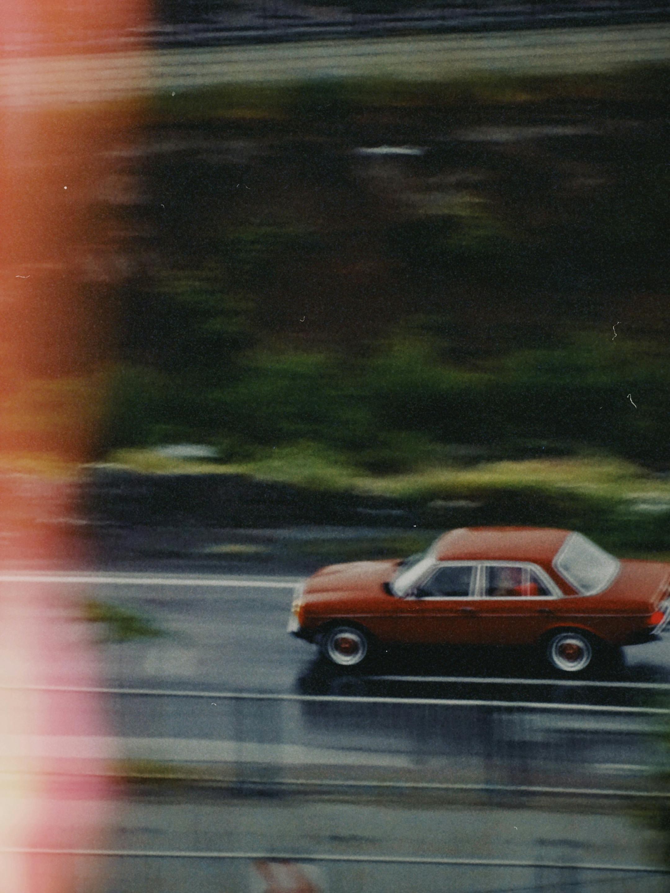 A defocused, vintage red car driving fast on a road in Kayseri, Türkiye.