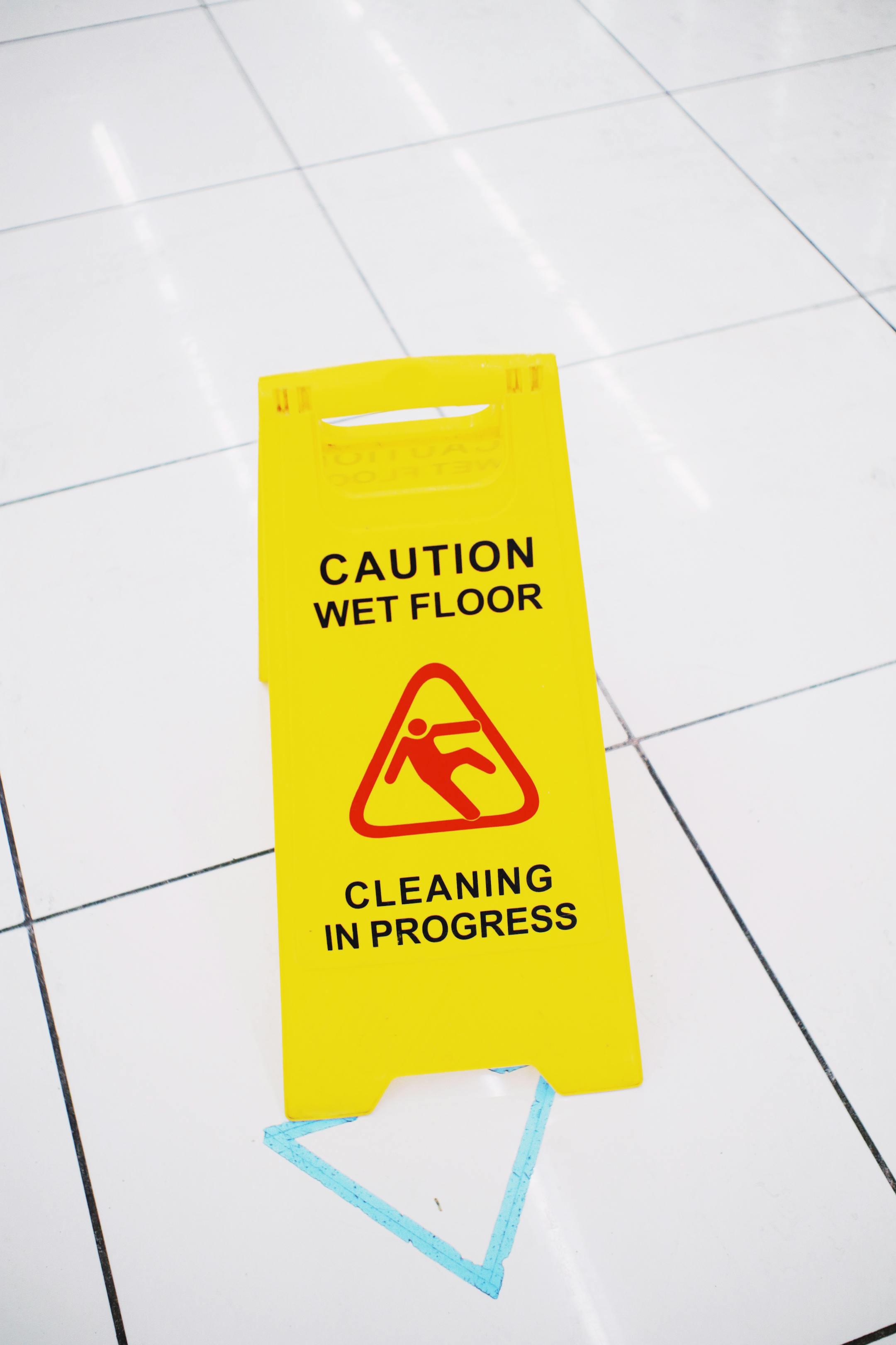 Bright yellow caution wet floor sign on white tiled floor indoors.