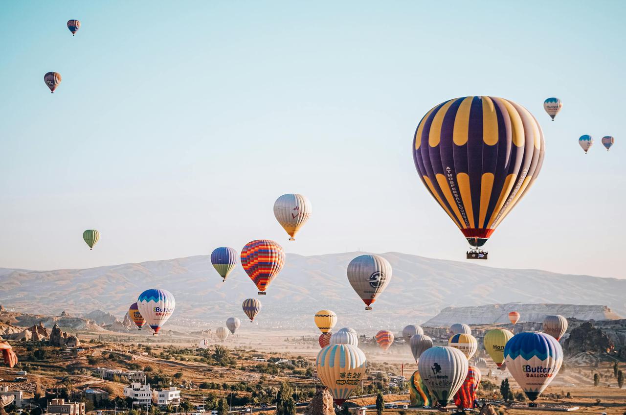 A scenic view of hot air balloons floating over Cappadocia, Türkiye at sunrise.