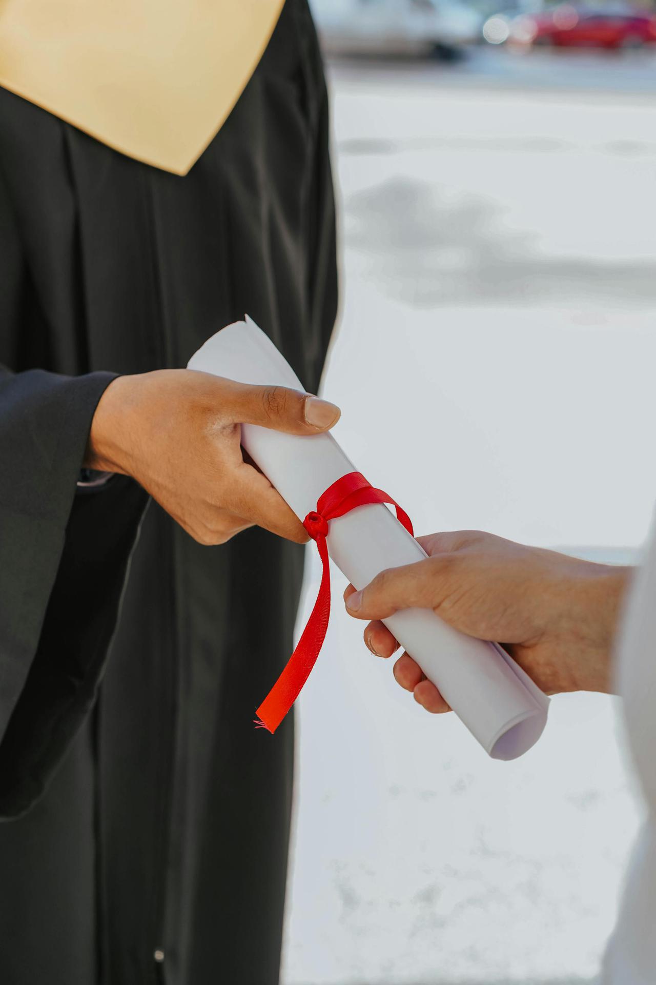 Hands exchanging a graduation diploma wrapped with red ribbon, symbolizing achievement.