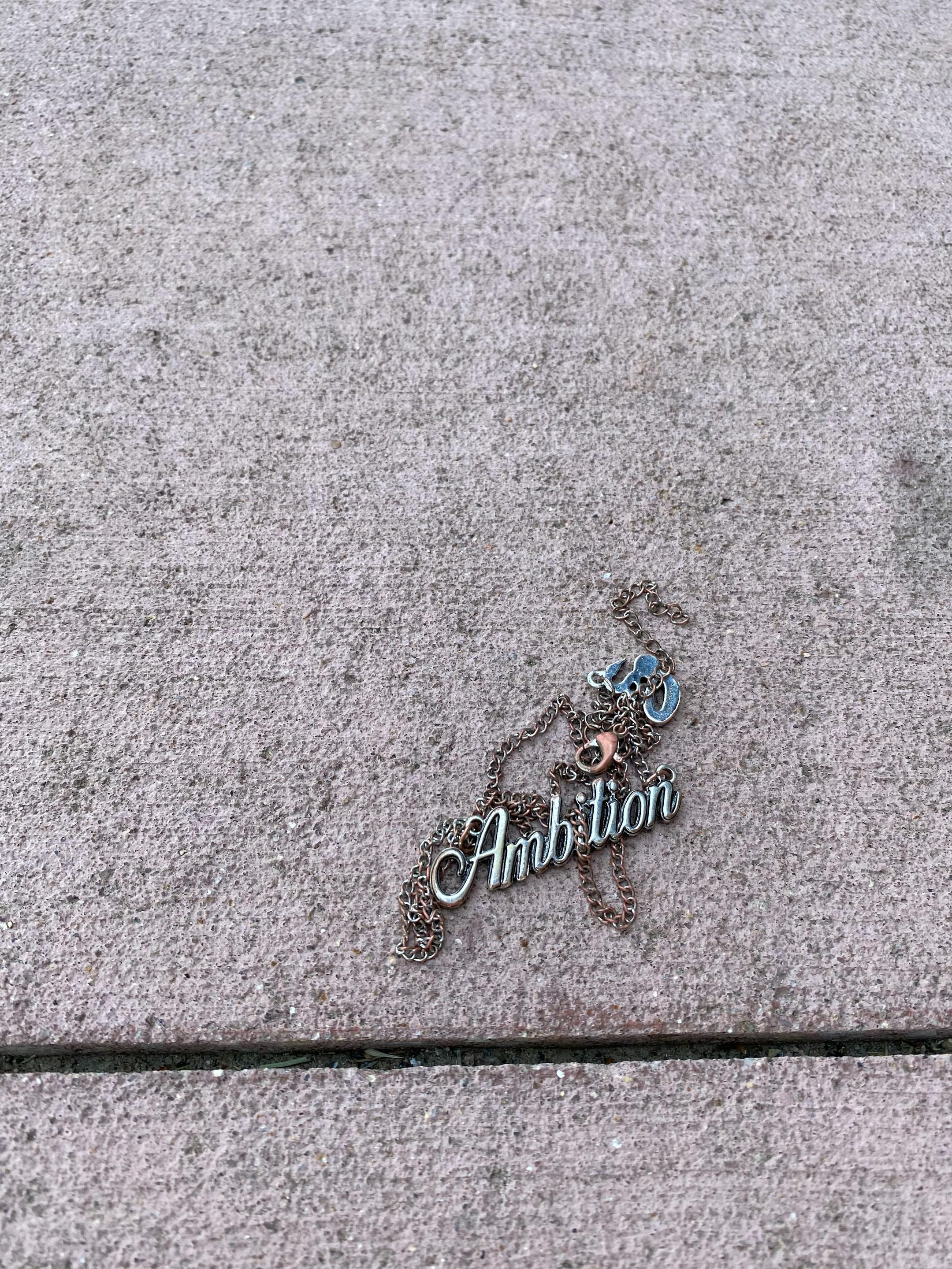 Broken “ambition” necklace on cement 