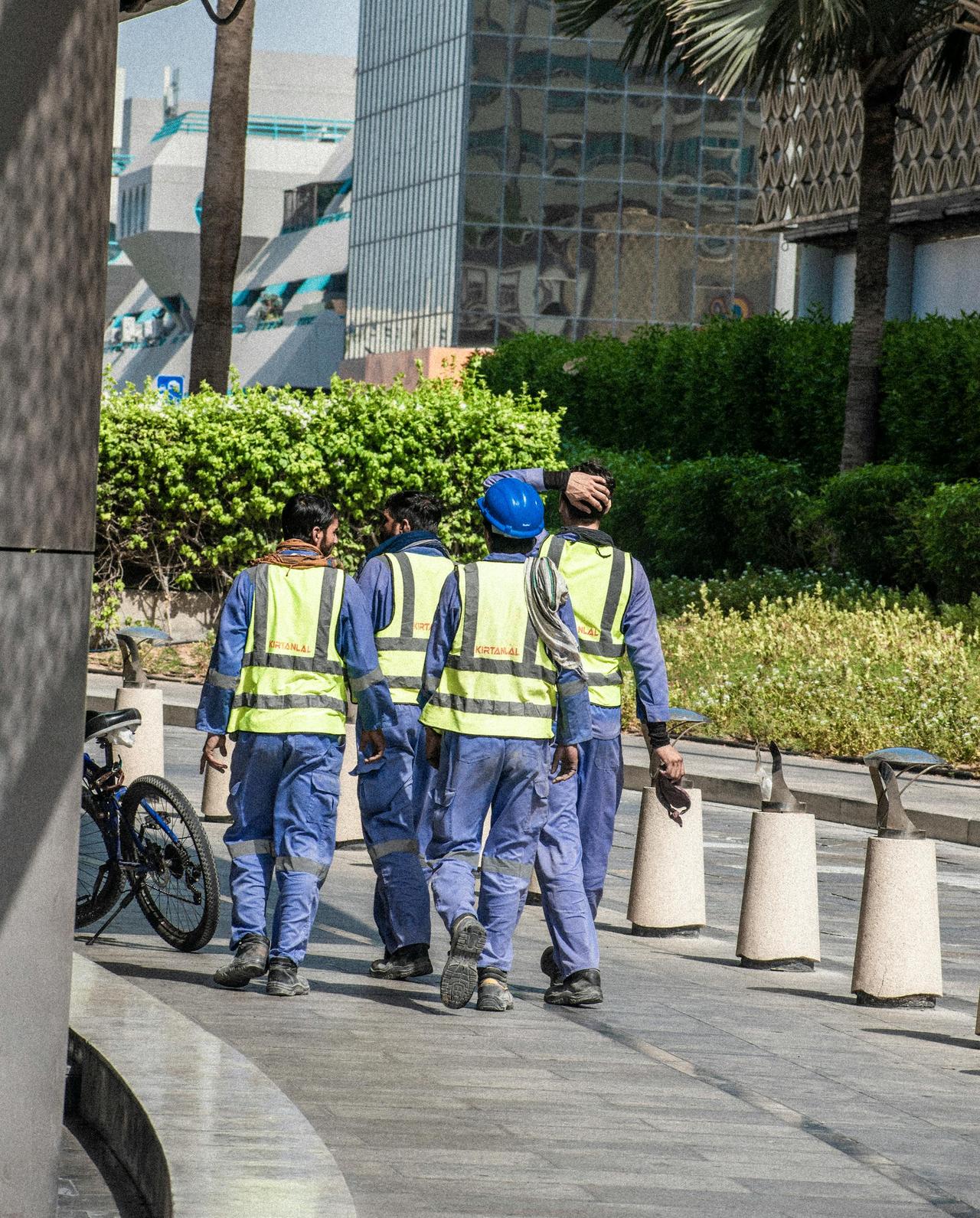 Group of workers wearing safety vests and helmets walking in a modern cityscape.