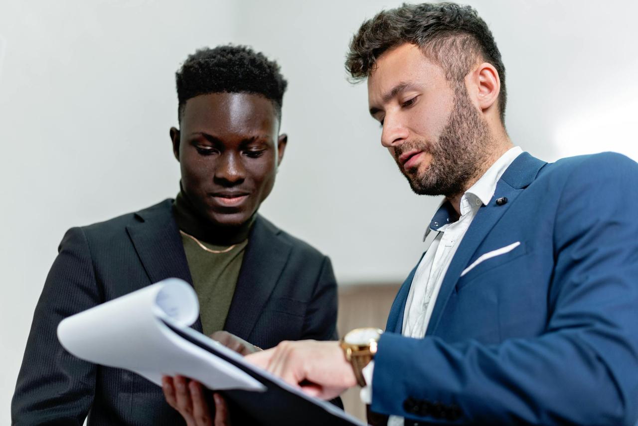 Two businessmen in suits discuss important documents in an office setting.